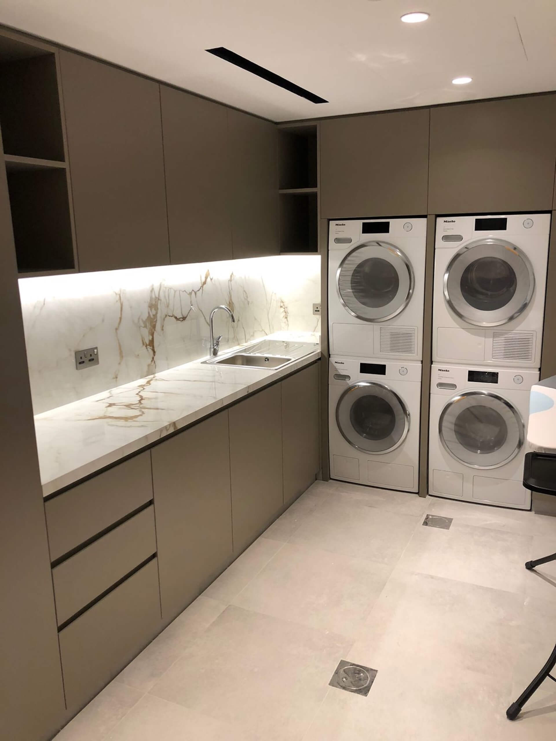 Modern laundry room with marble countertop, sink, and four stacked white dryers