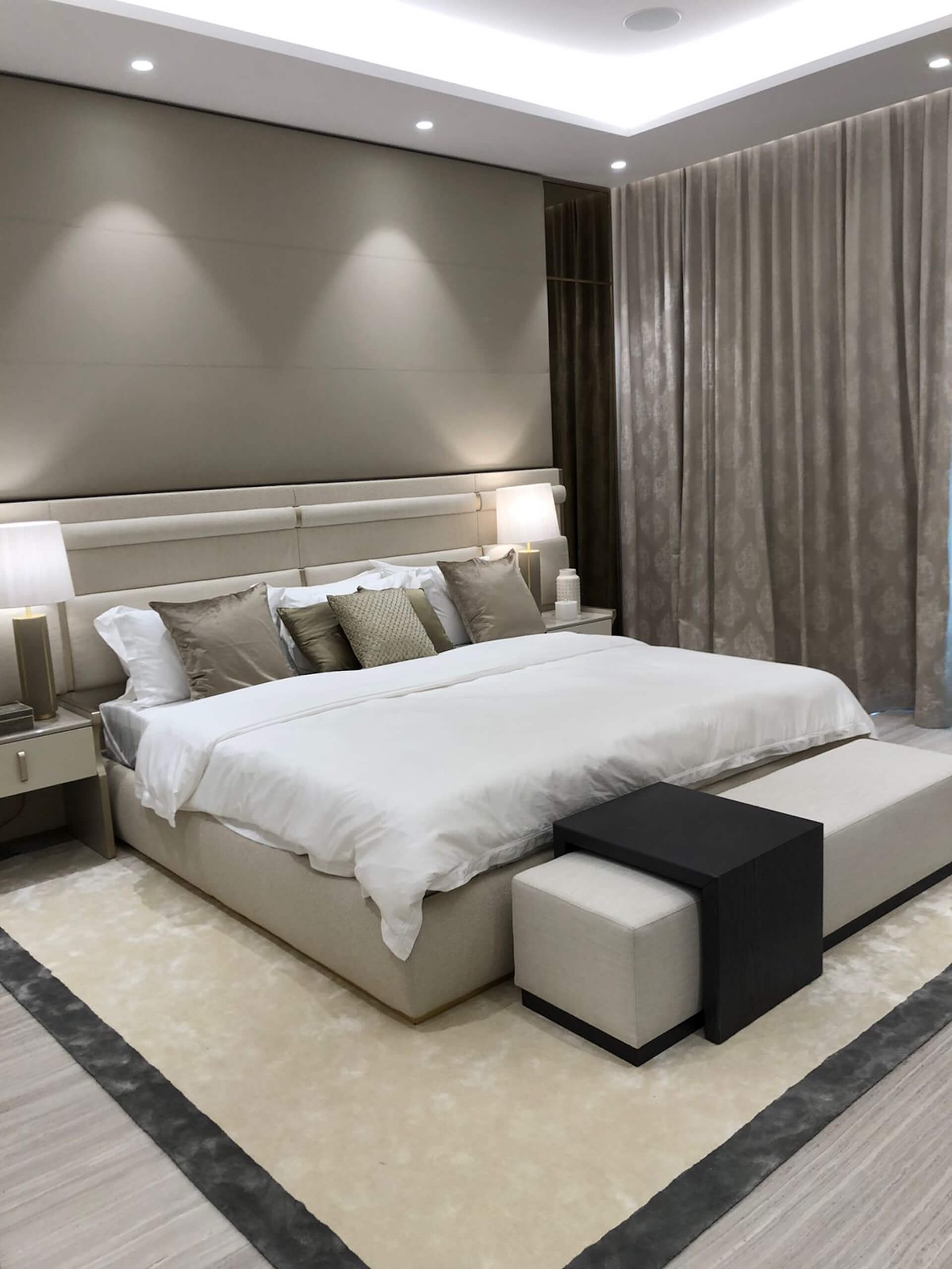 Modern luxury bedroom with white upholstered bed, neutral decor, and floor-to-ceiling curtains.