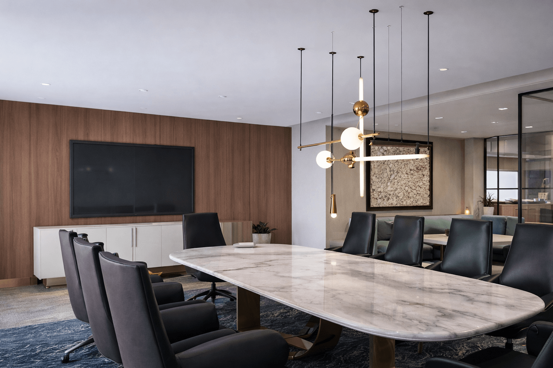 Modern conference room with marble table, black leather chairs, and large wall-mounted display screen.