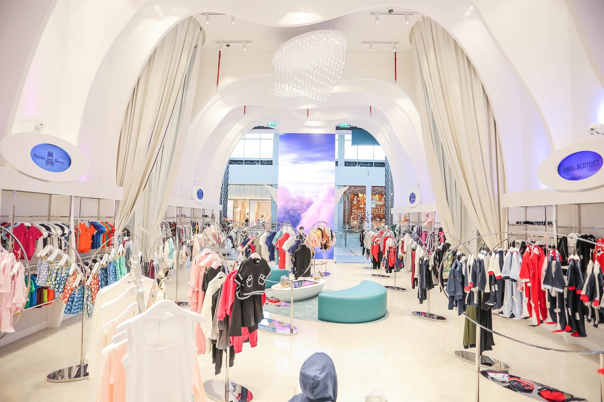 Modern children's clothing boutique with arched white ceiling, colorful garments displayed on racks throughout