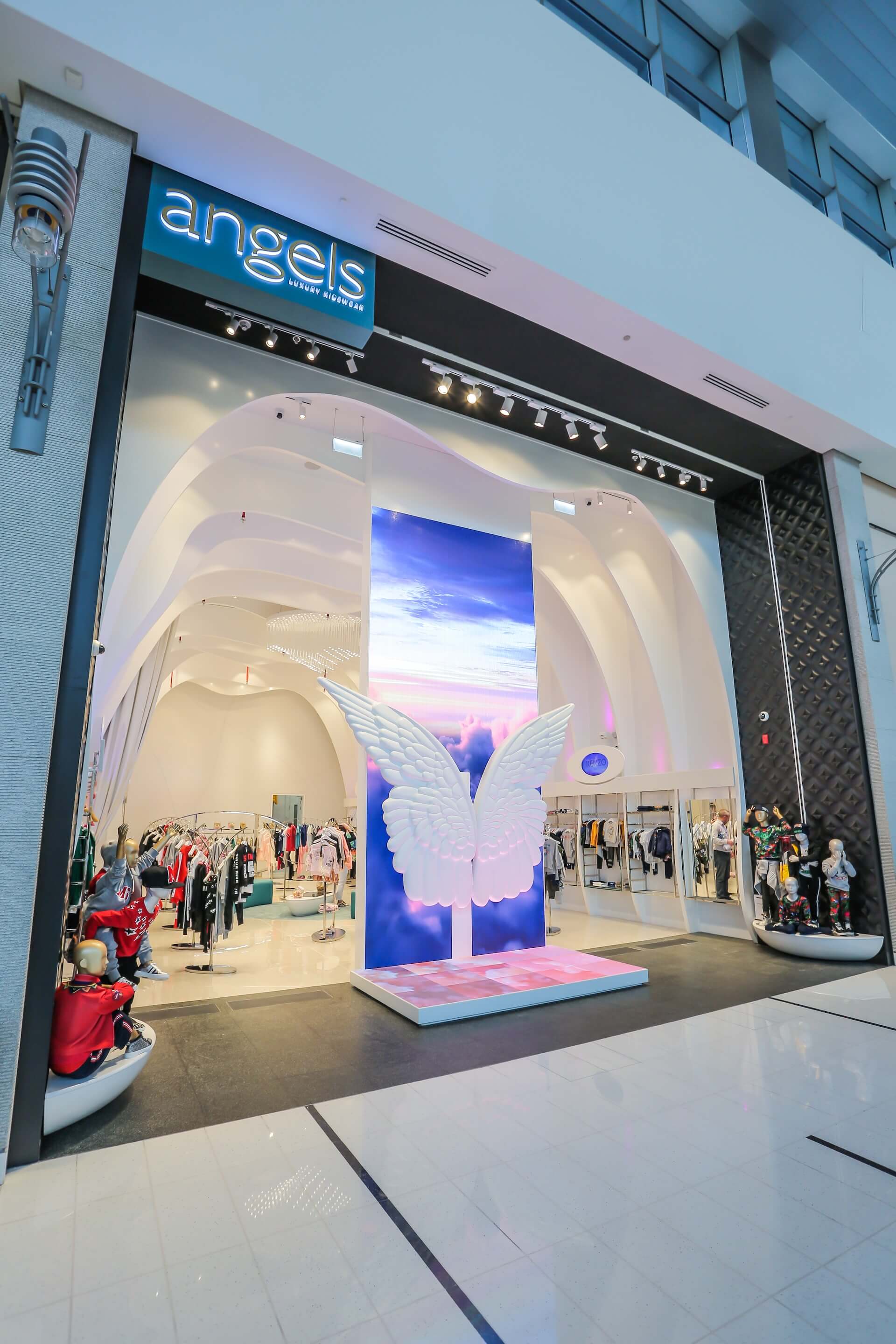 Angels luxury fashion boutique storefront with large white wing installation and colorful lighting display