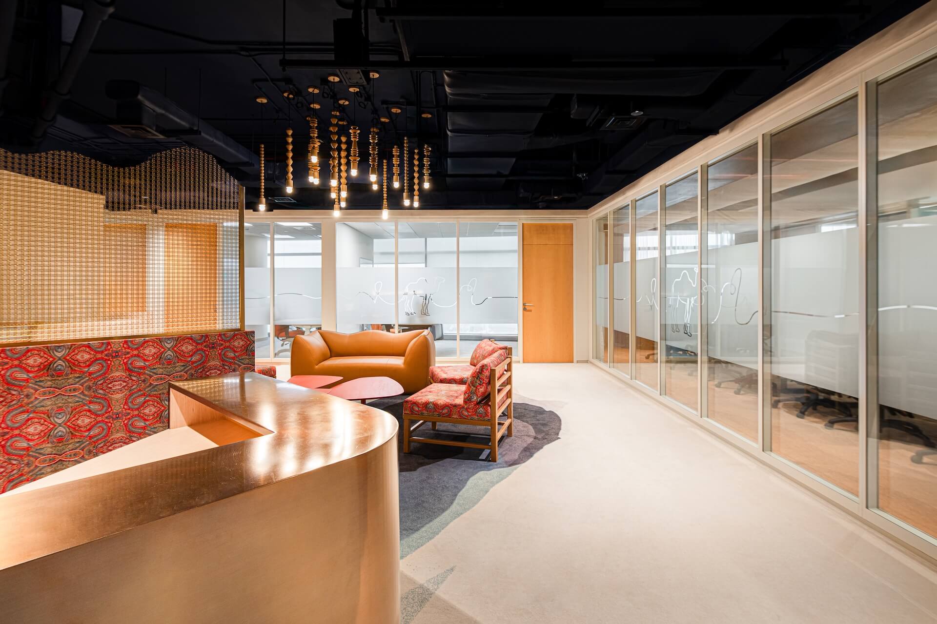Modern office lounge with orange furniture, wood accents, and glass partition walls