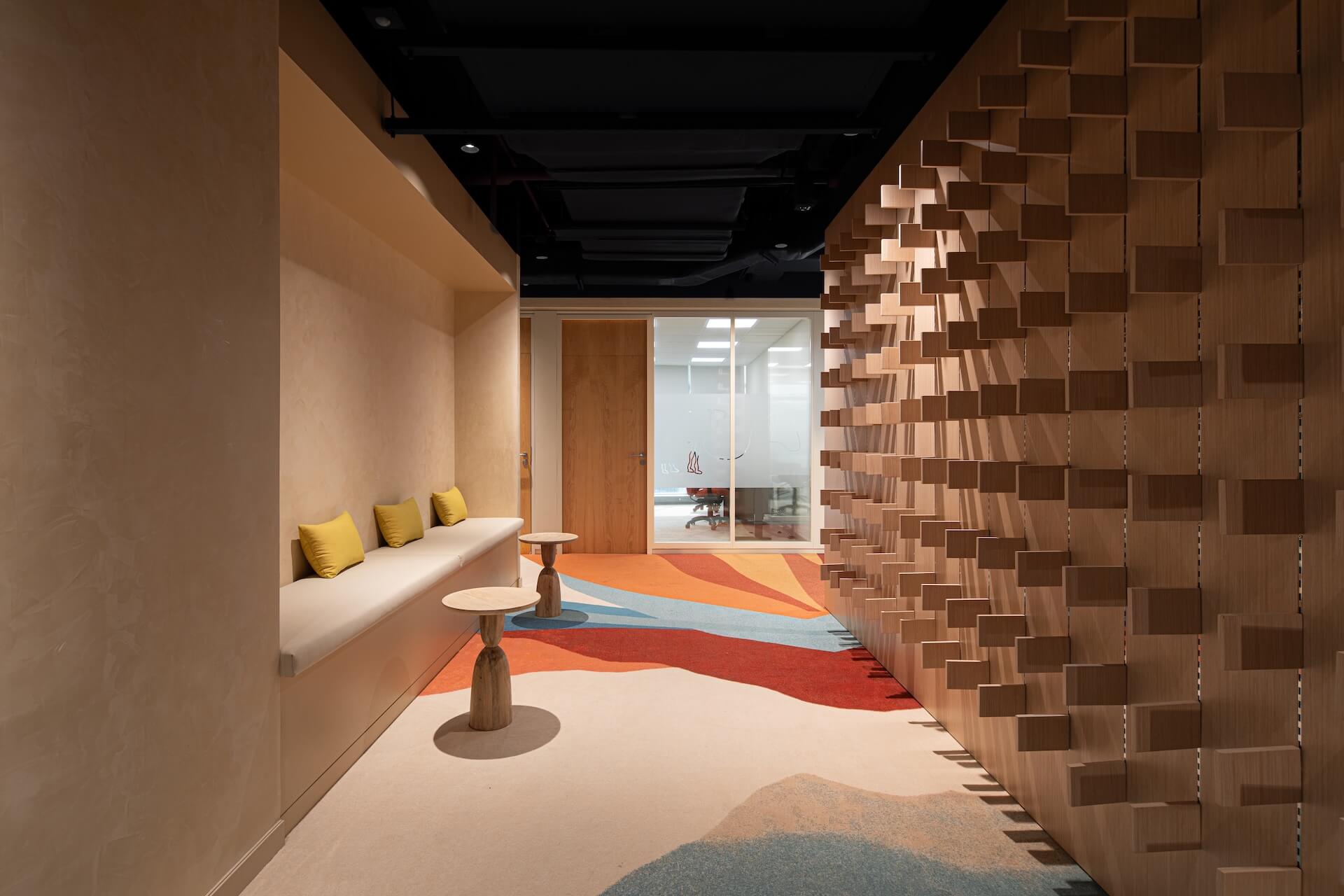 Modern office corridor with wooden brick wall, colorful floor, window seating, and glass entrance.