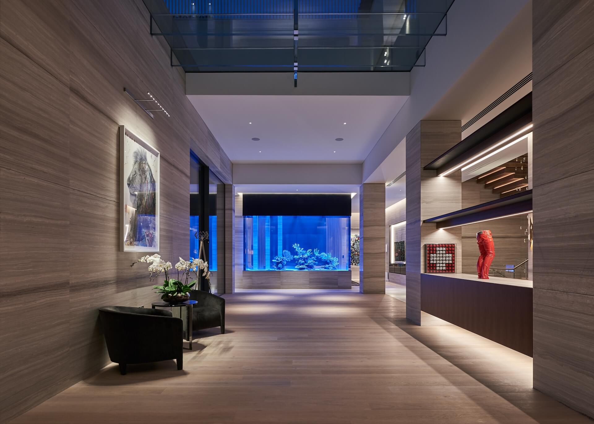 Modern luxury hallway with illuminated aquarium, wood walls, artwork, and contemporary furniture.