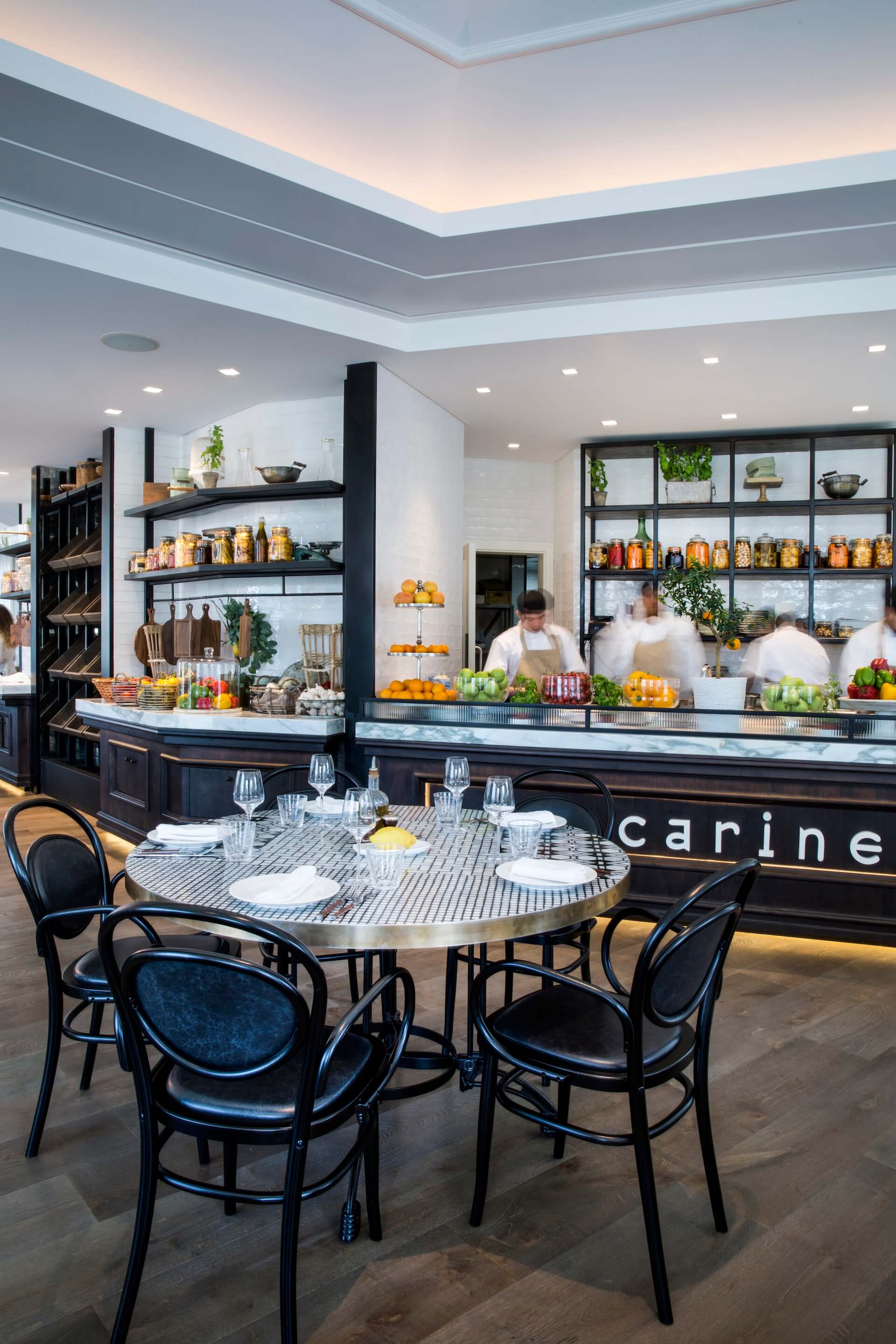 Modern restaurant dining area with set table, open kitchen, and staff preparing food behind counter
