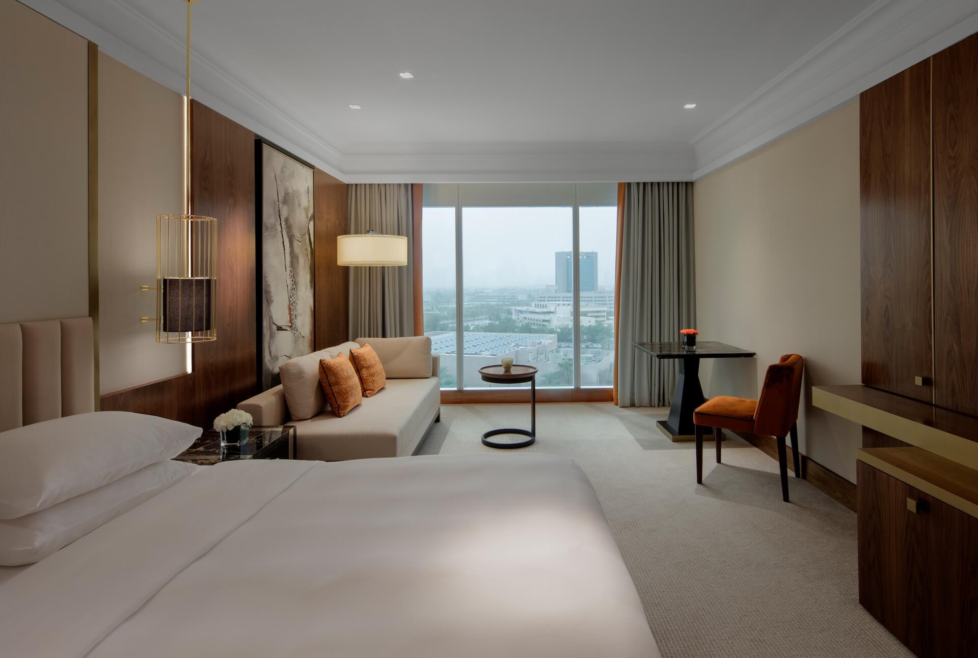 Modern luxury hotel room with bed, sofa, city skyline view through floor-to-ceiling windows