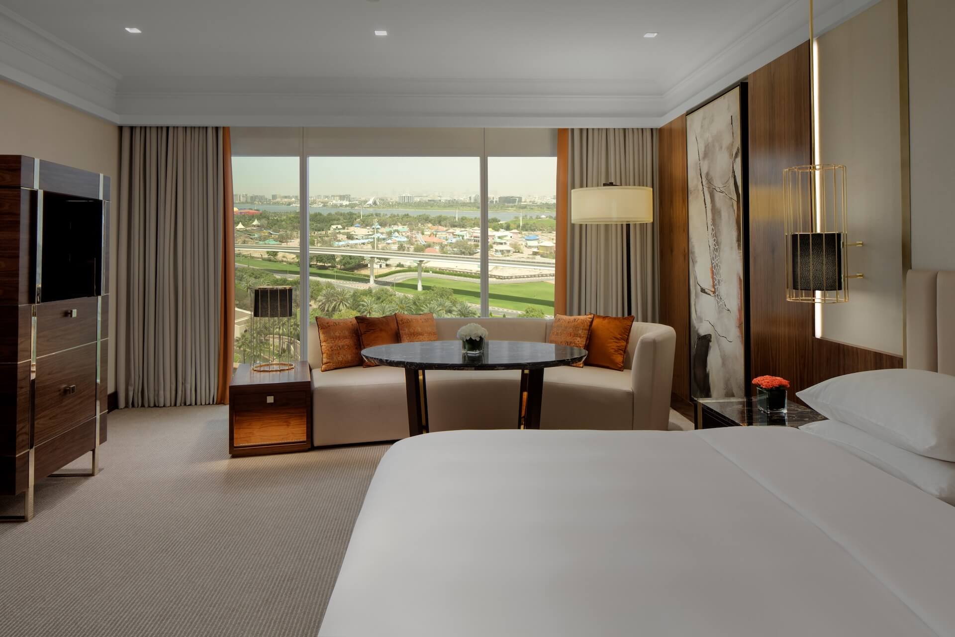 Modern luxury hotel suite with cityscape view, beige sofa, wood accents, and panoramic windows