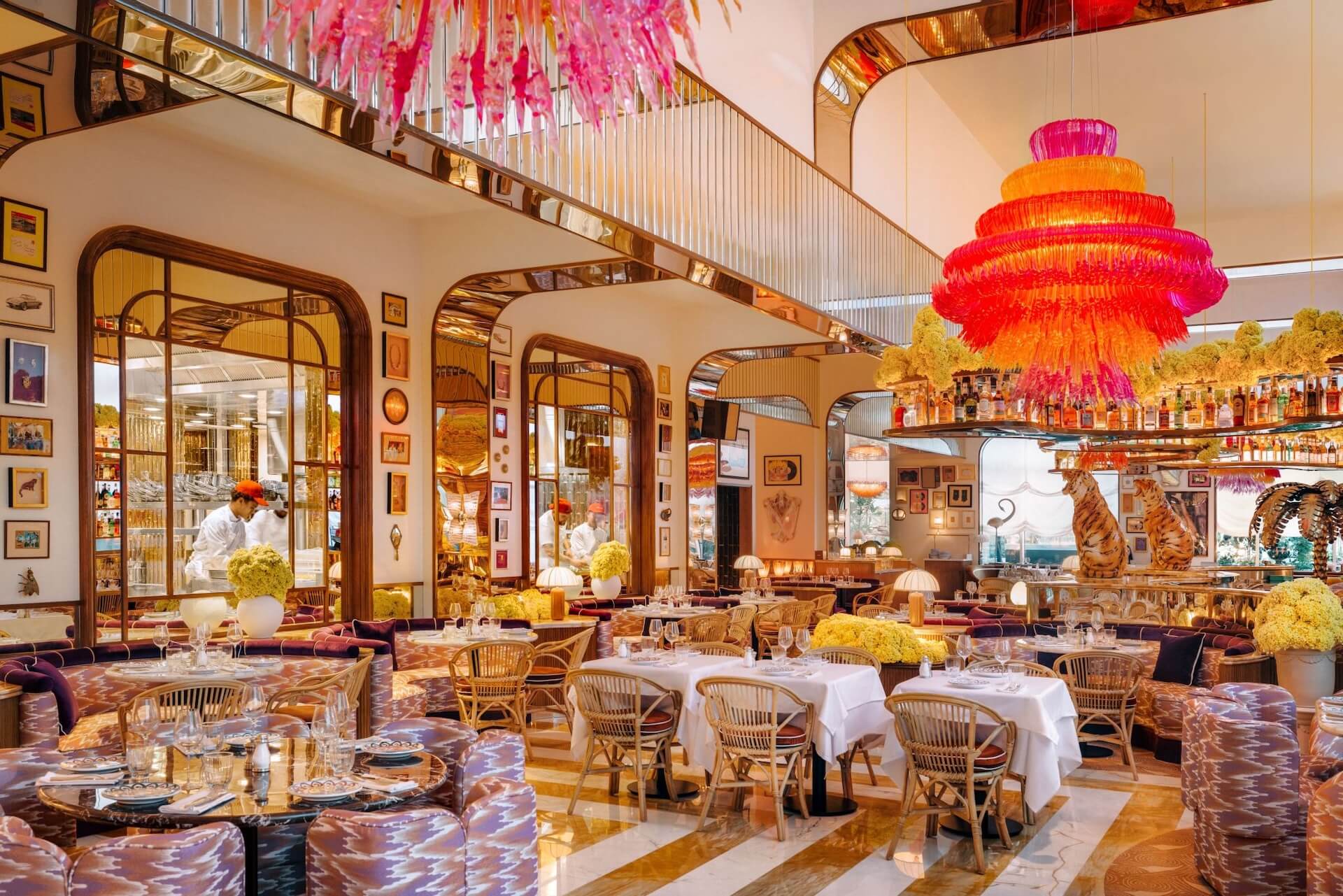 Luxurious restaurant interior with colorful chandeliers, elegant dining tables, and decorative floral arrangements.
