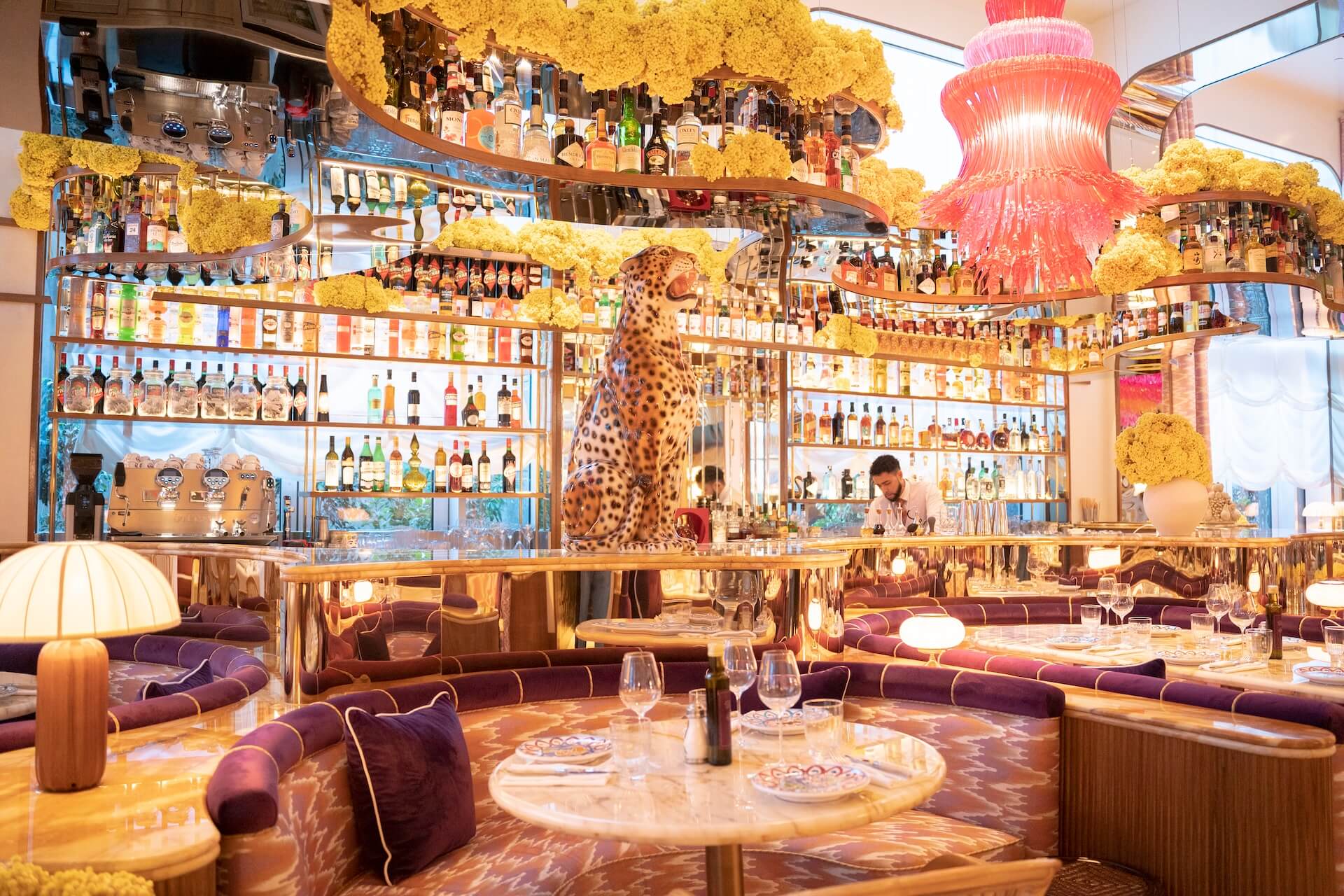 Luxury bar and lounge with extensive bottle display, leopard statue, yellow floral decor, purple seating.