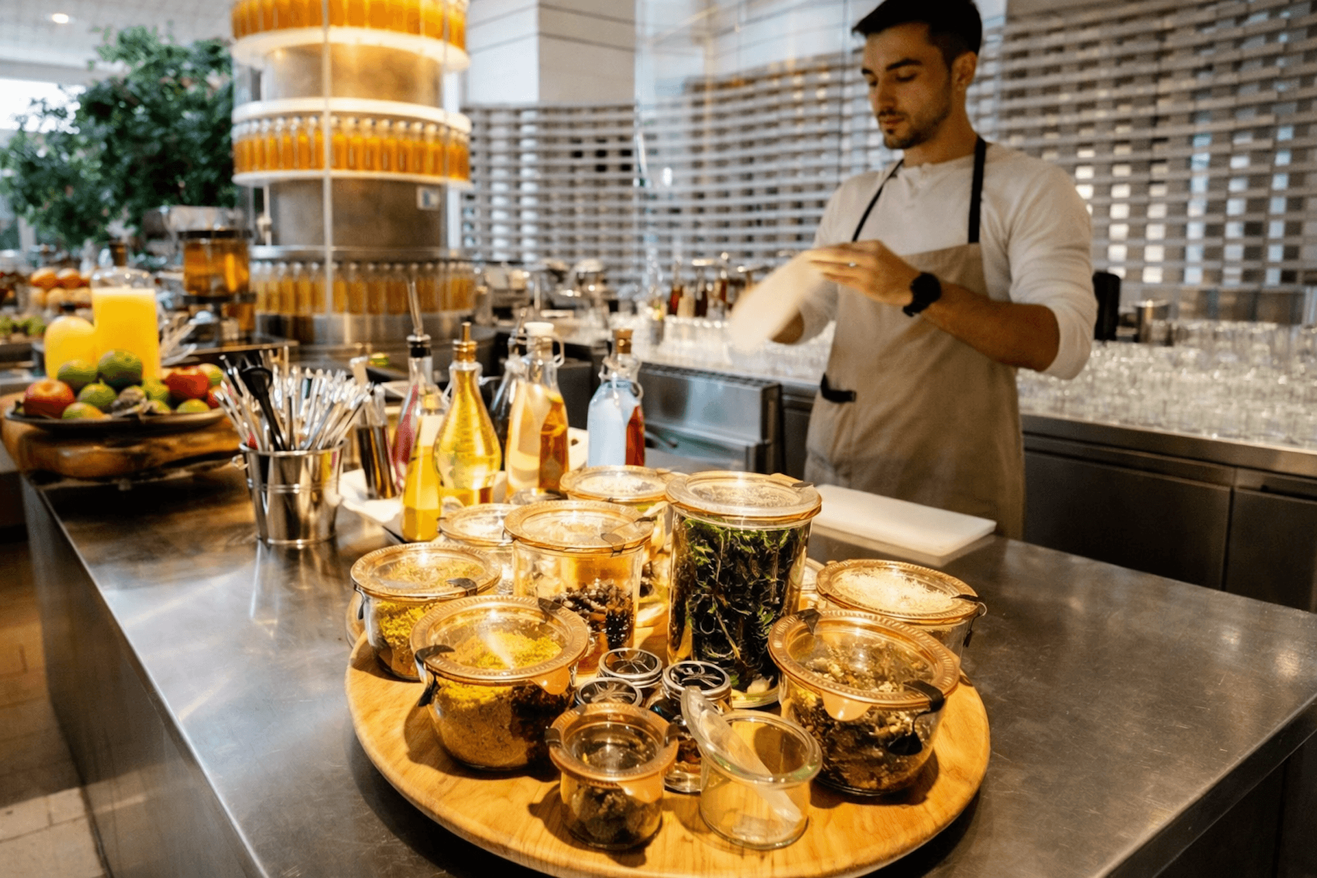 Chef preparing gourmet tea in modern kitchen with glass jars and infusions displayed on counter.