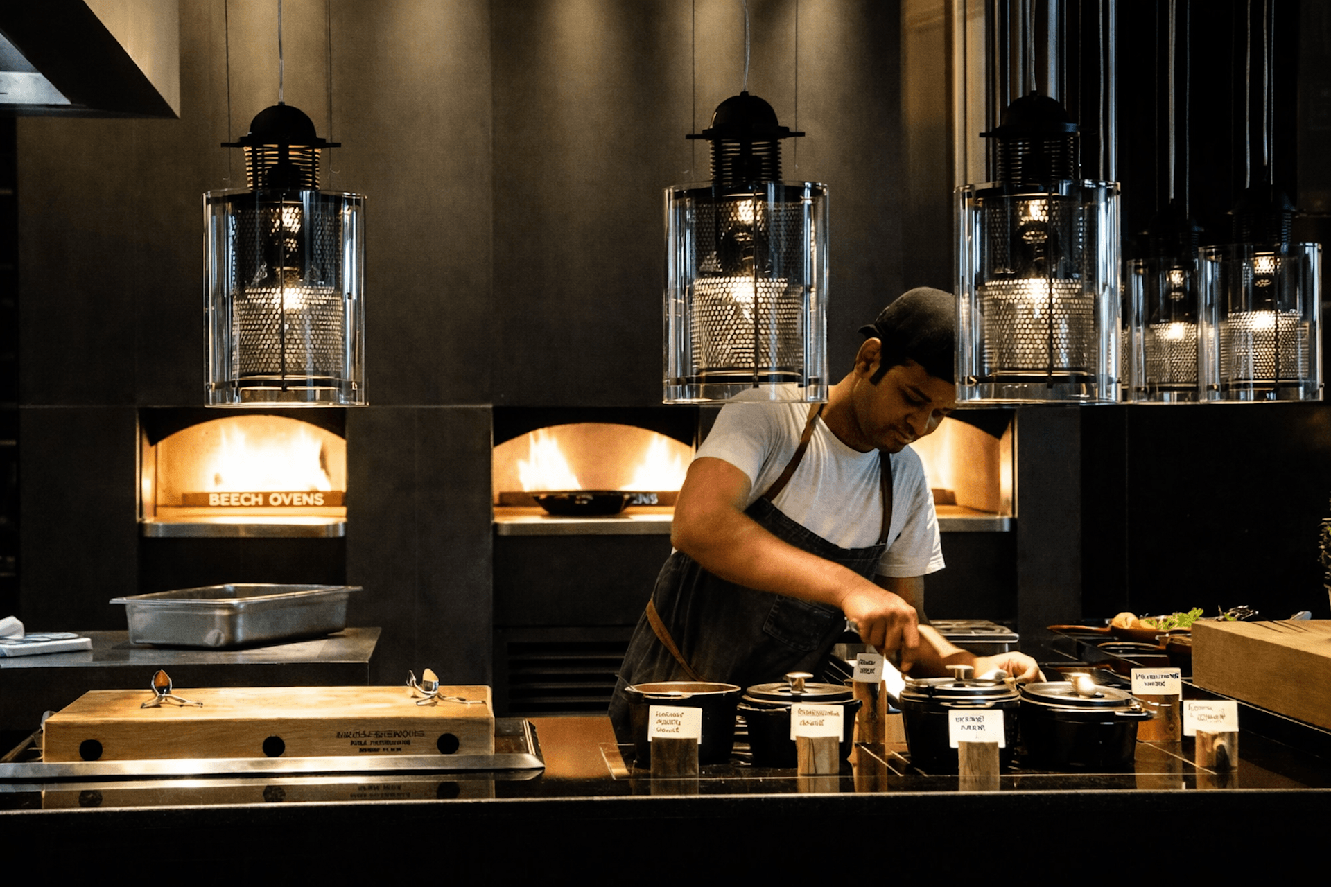 Chef preparing food in modern open kitchen with pendant lights and Beech ovens