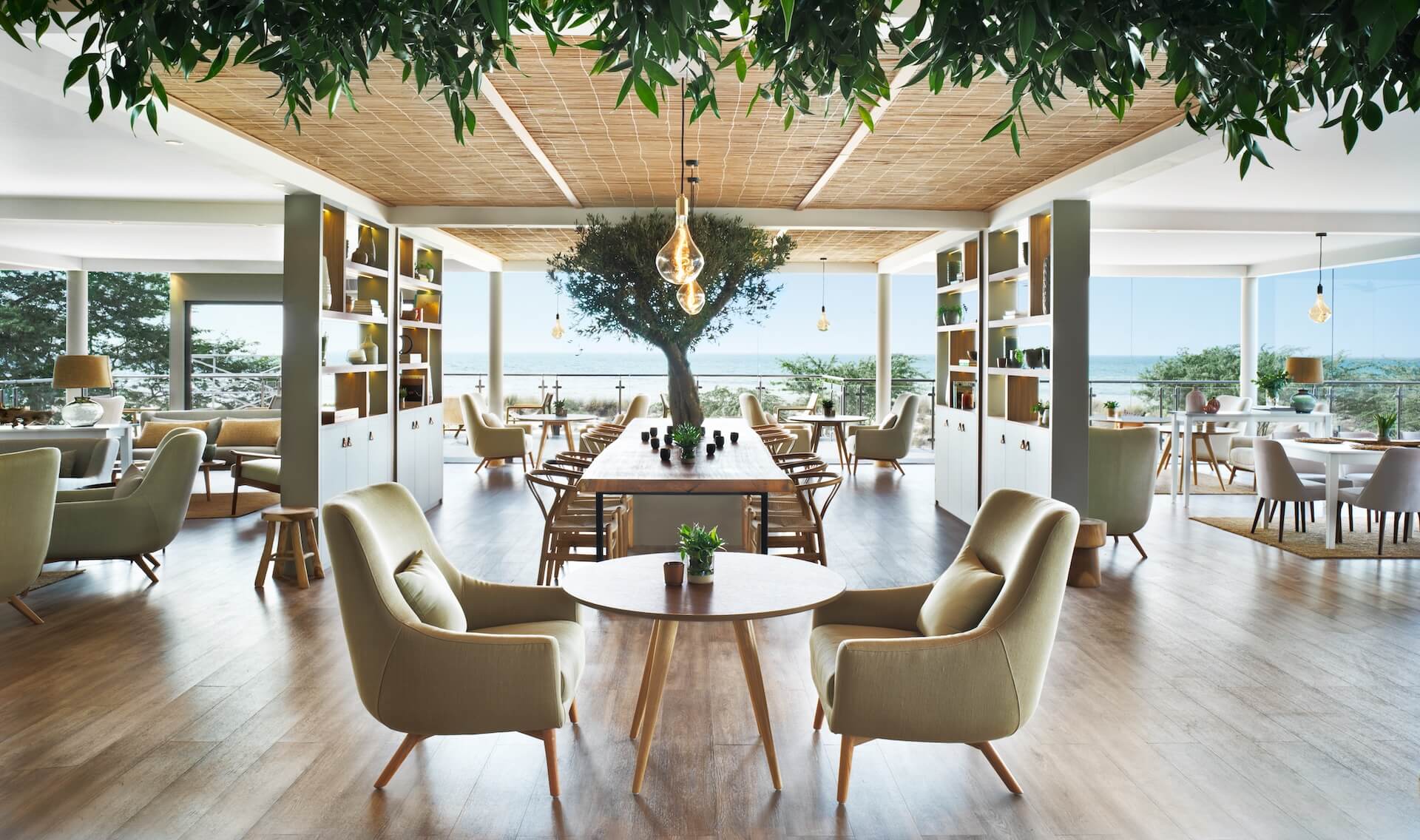 Modern luxury interior with hanging greenery, seating areas, dining table, ocean view