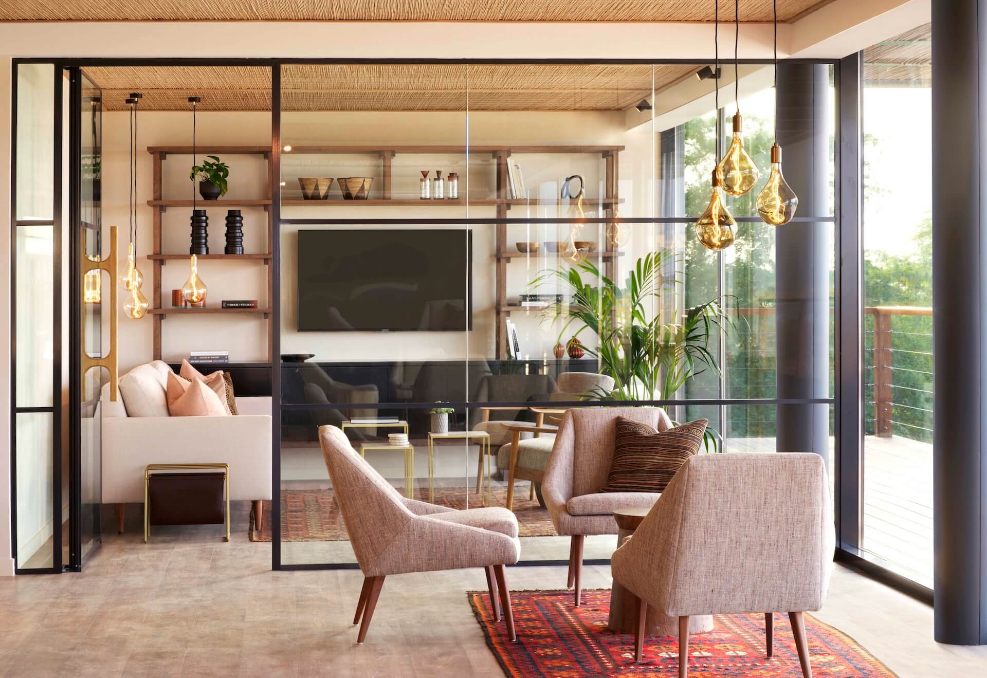 Modern living room with pink armchairs, wooden shelving, pendant lights, and glass partitions