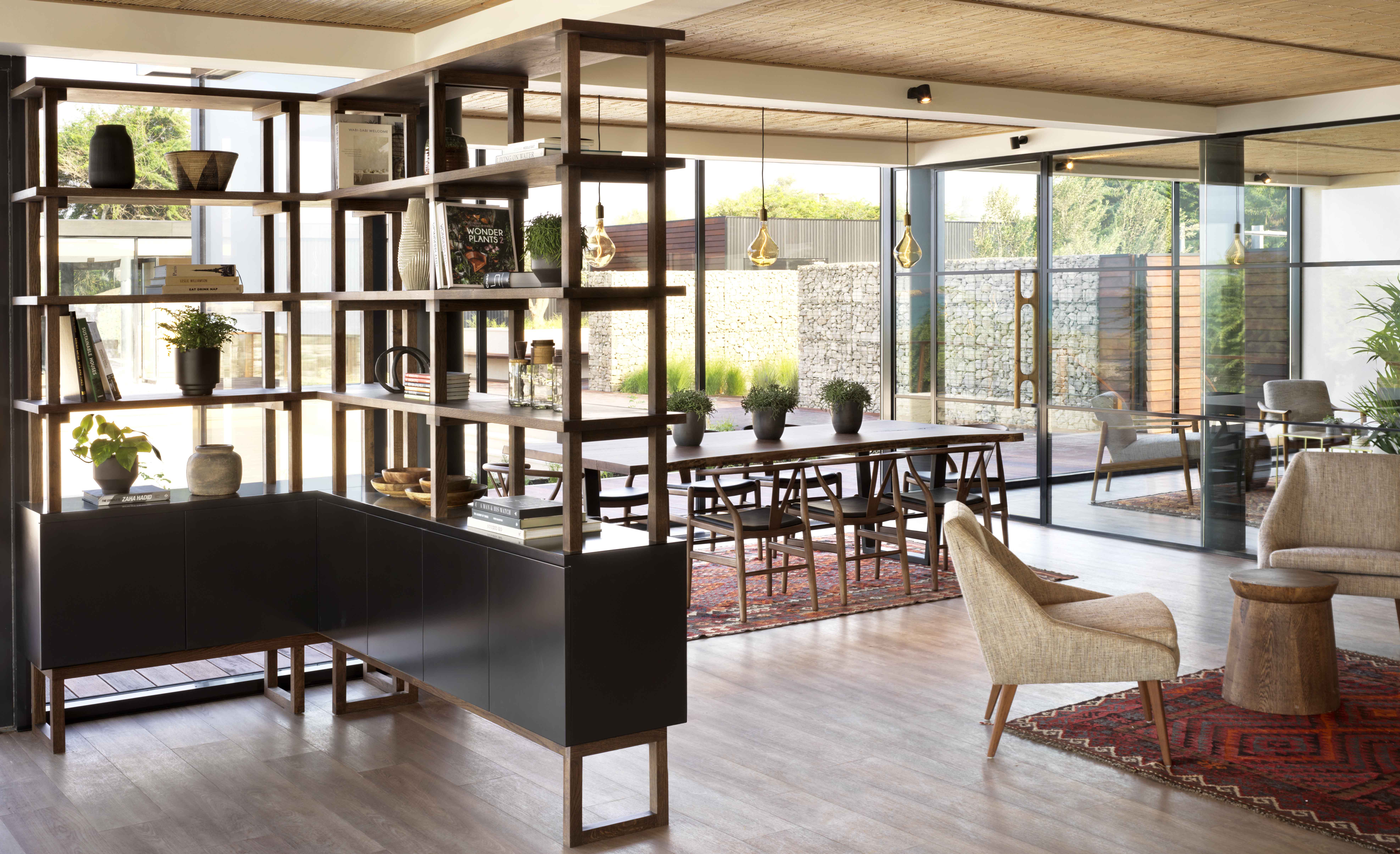 Modern open-plan living space with wooden shelving, dining area, and outdoor patio view