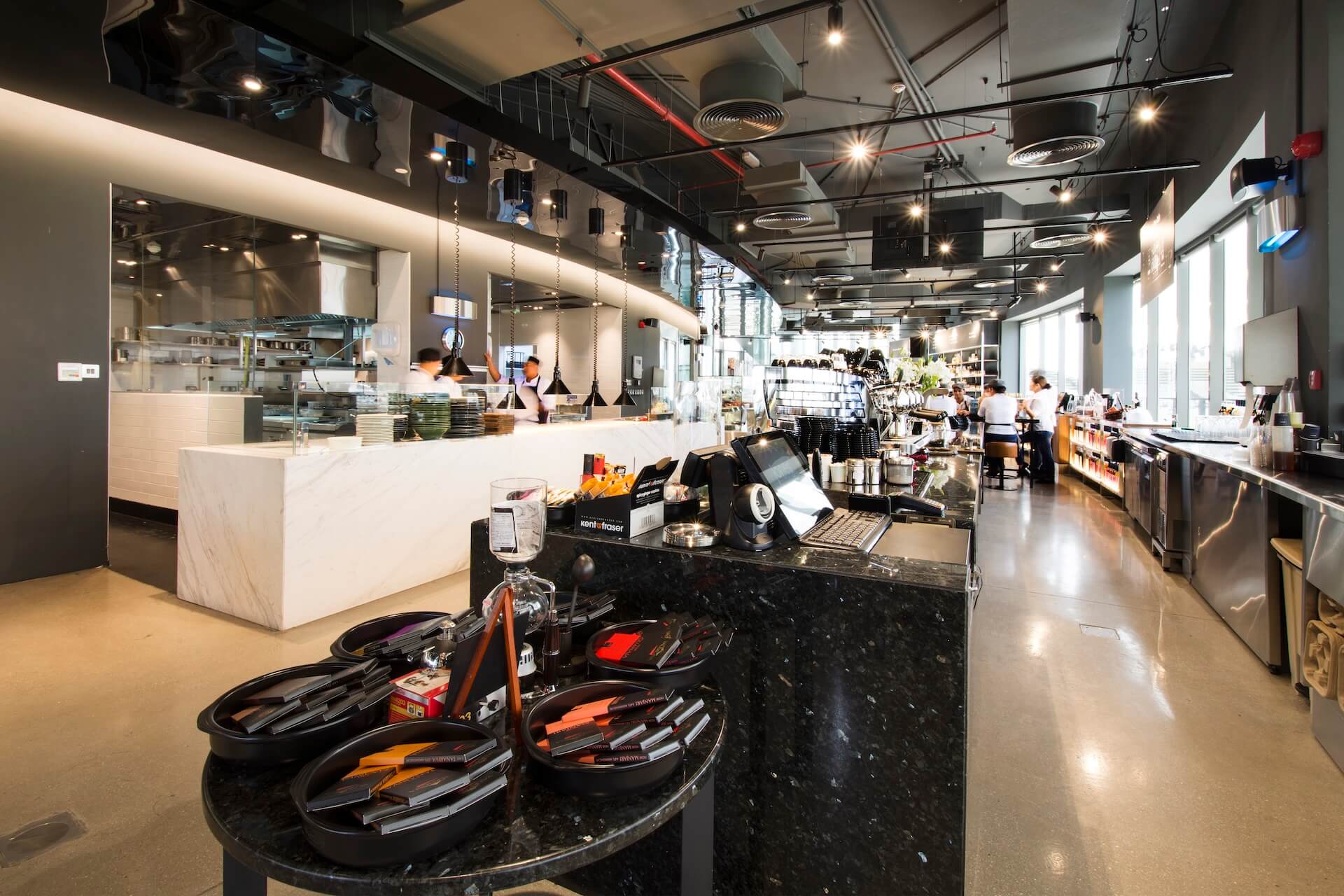 Modern kitchen showroom with white marble counter, black display island with tools, customers and staff throughout the bright space