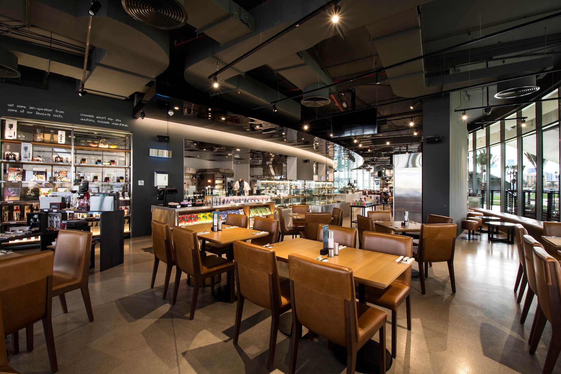 Modern cafe interior with tan leather seating, wooden tables, and product display counter.