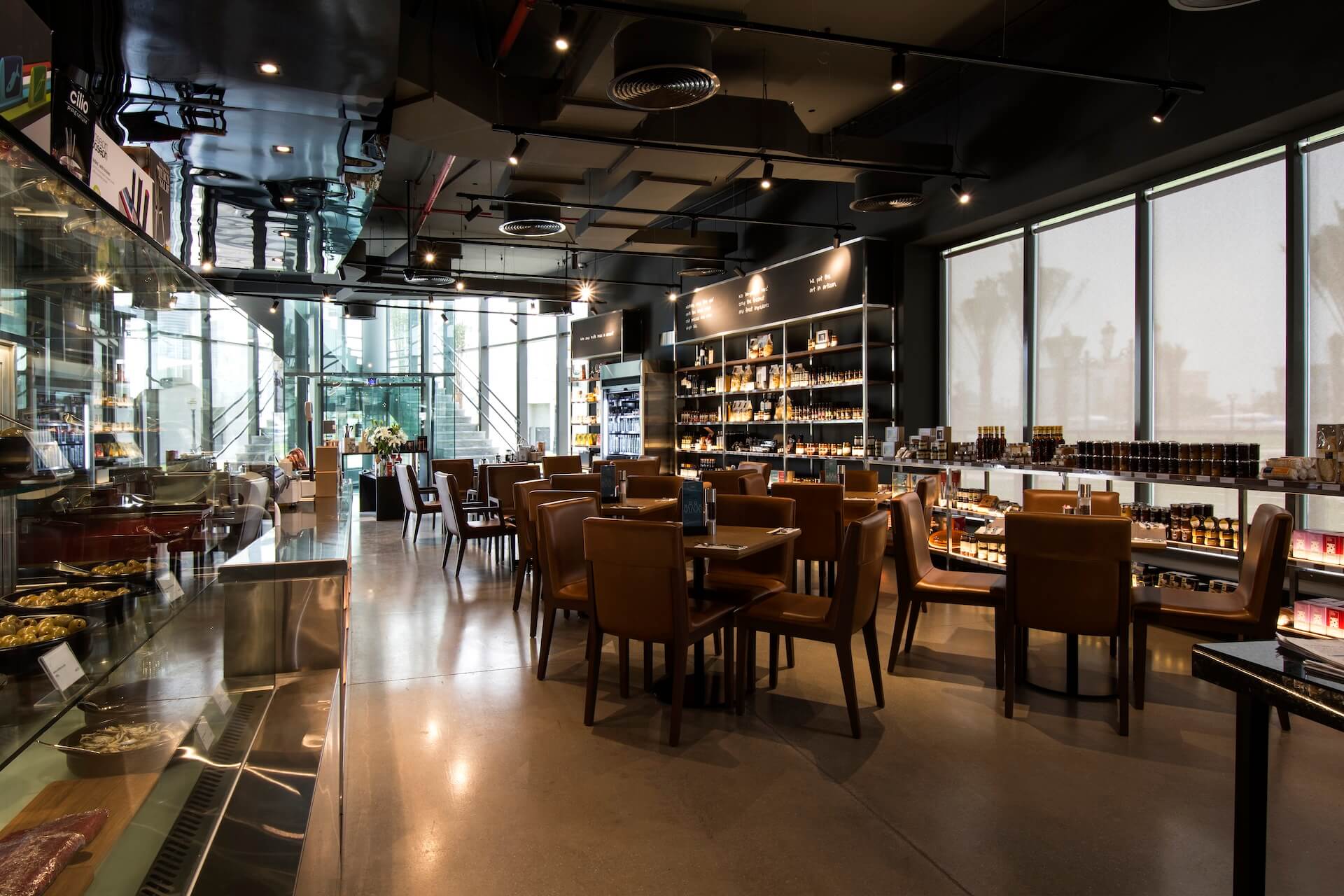 Modern upscale café with brown leather chairs, shelving displays, floor-to-ceiling windows, and city views
