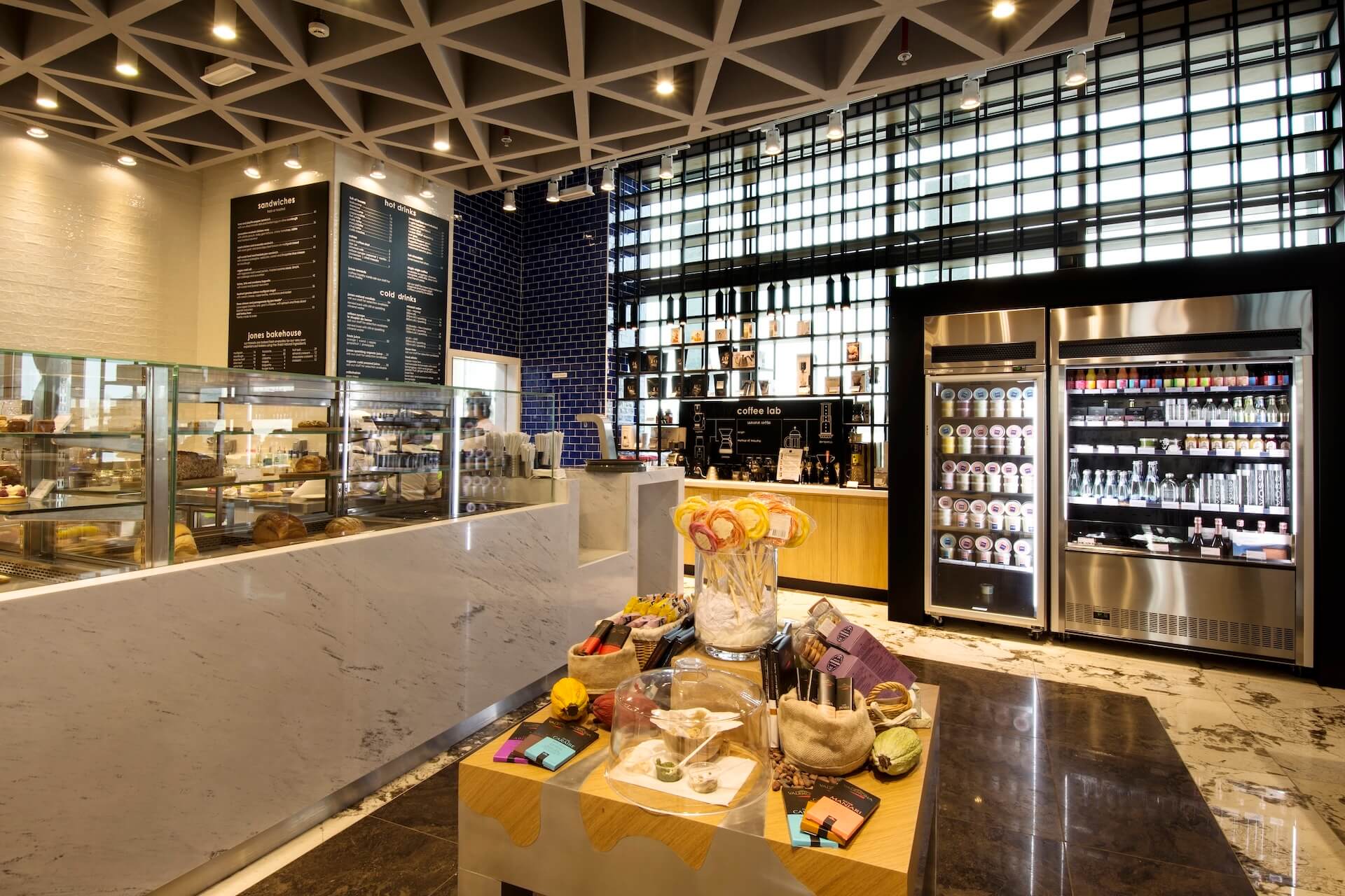 Modern cafe interior with marble counter, menu boards, refreshment display, and product showcase refrigerator.