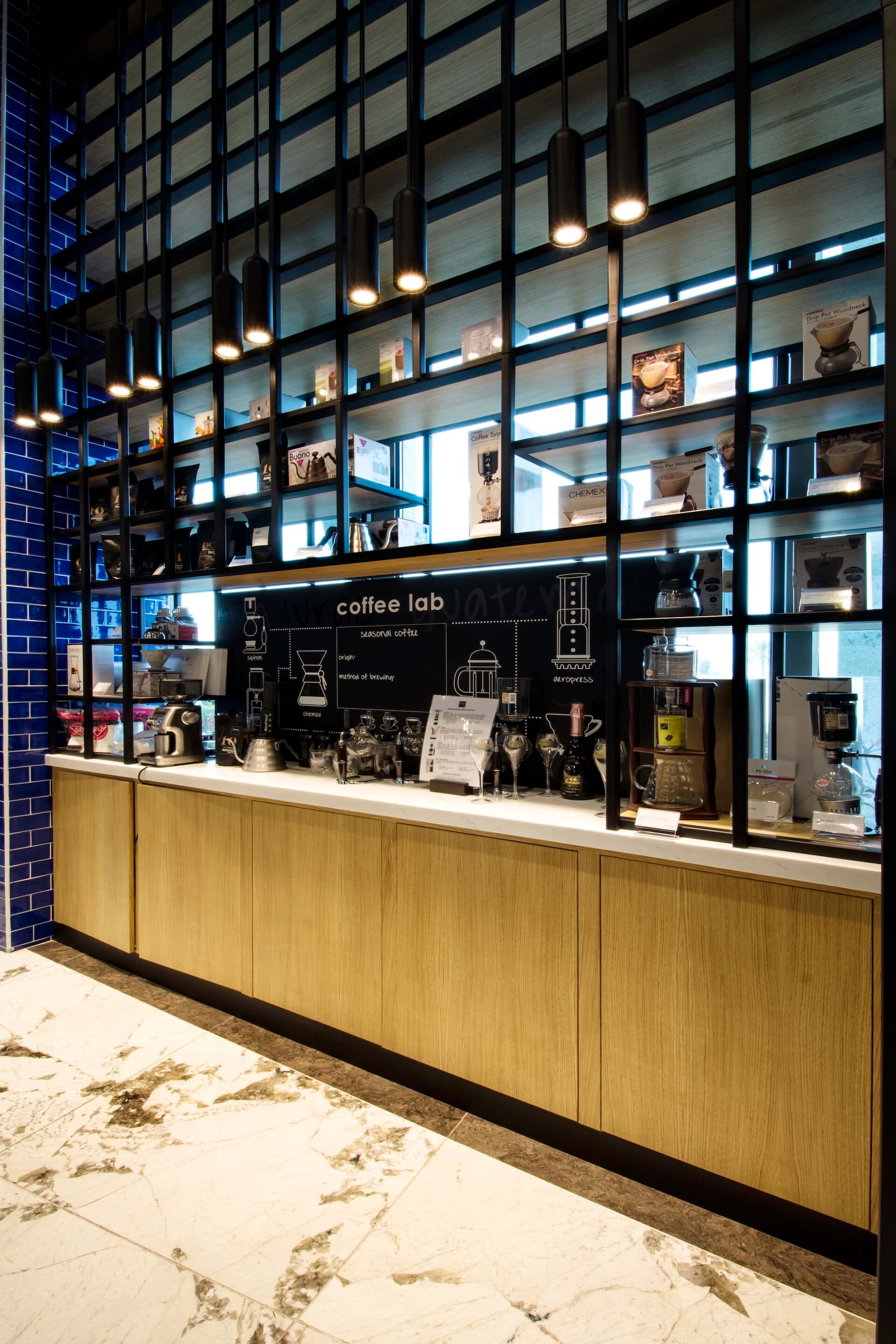 Modern coffee lab display with wooden counter, shelving unit, equipment, and blue brick wall