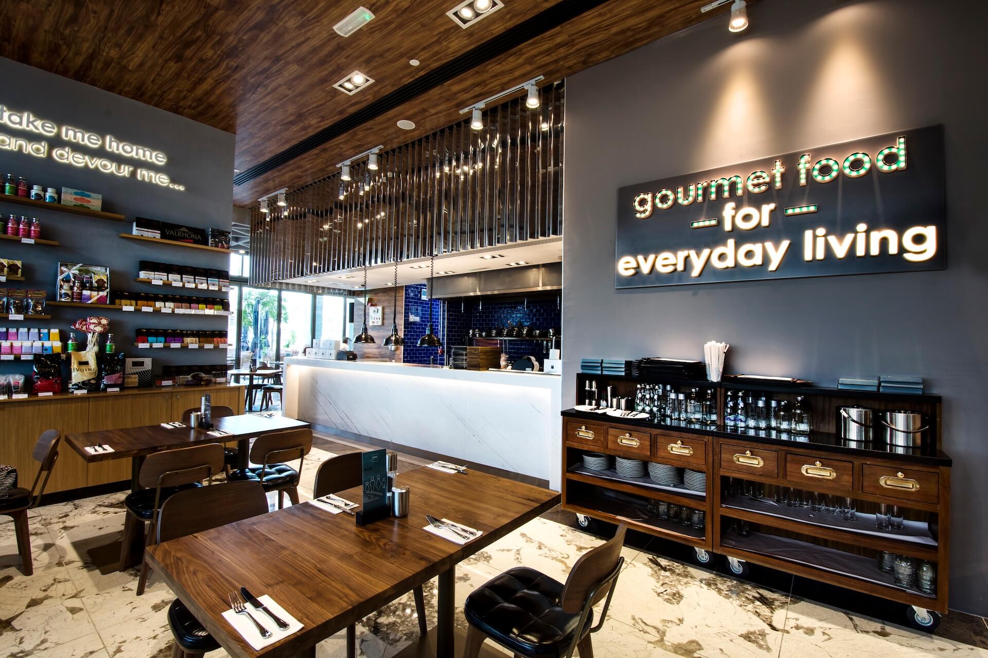 Modern gourmet restaurant interior with wood ceiling, white counter, neon signage, and dining tables.