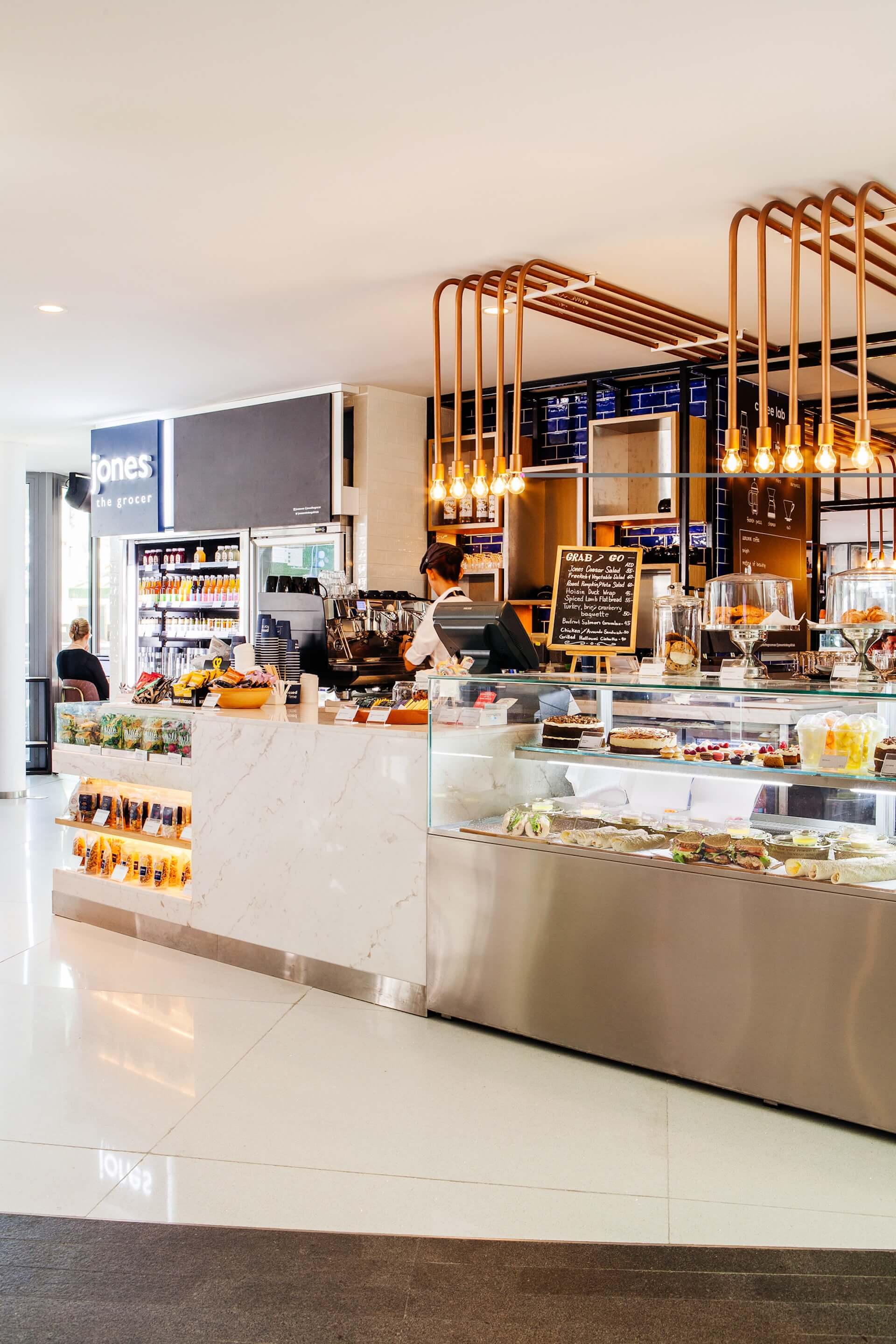 Modern café interior with marble counter, display cases, copper fixtures, and barista at coffee machine.