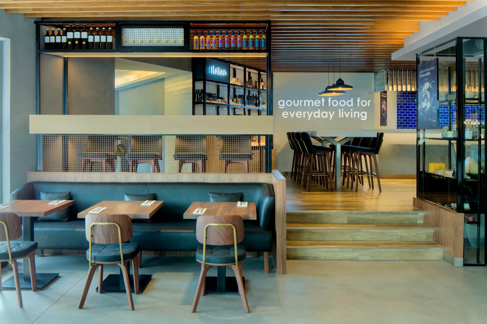 Modern restaurant interior with teal banquette seating, counter service, and "gourmet food for everyday living" signage