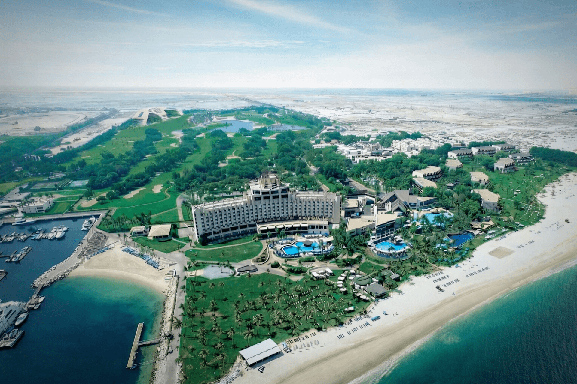 Aerial view of a beachfront resort with pools, palm trees, and sandy coastline beside turquoise water
