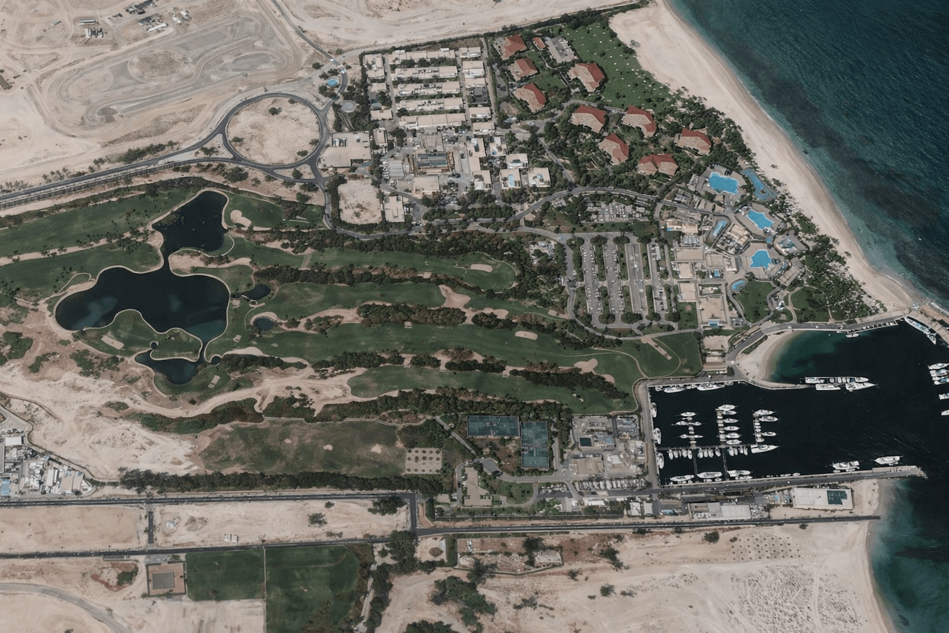 Aerial view of coastal resort development with golf course, marina, hotels, and residential villas