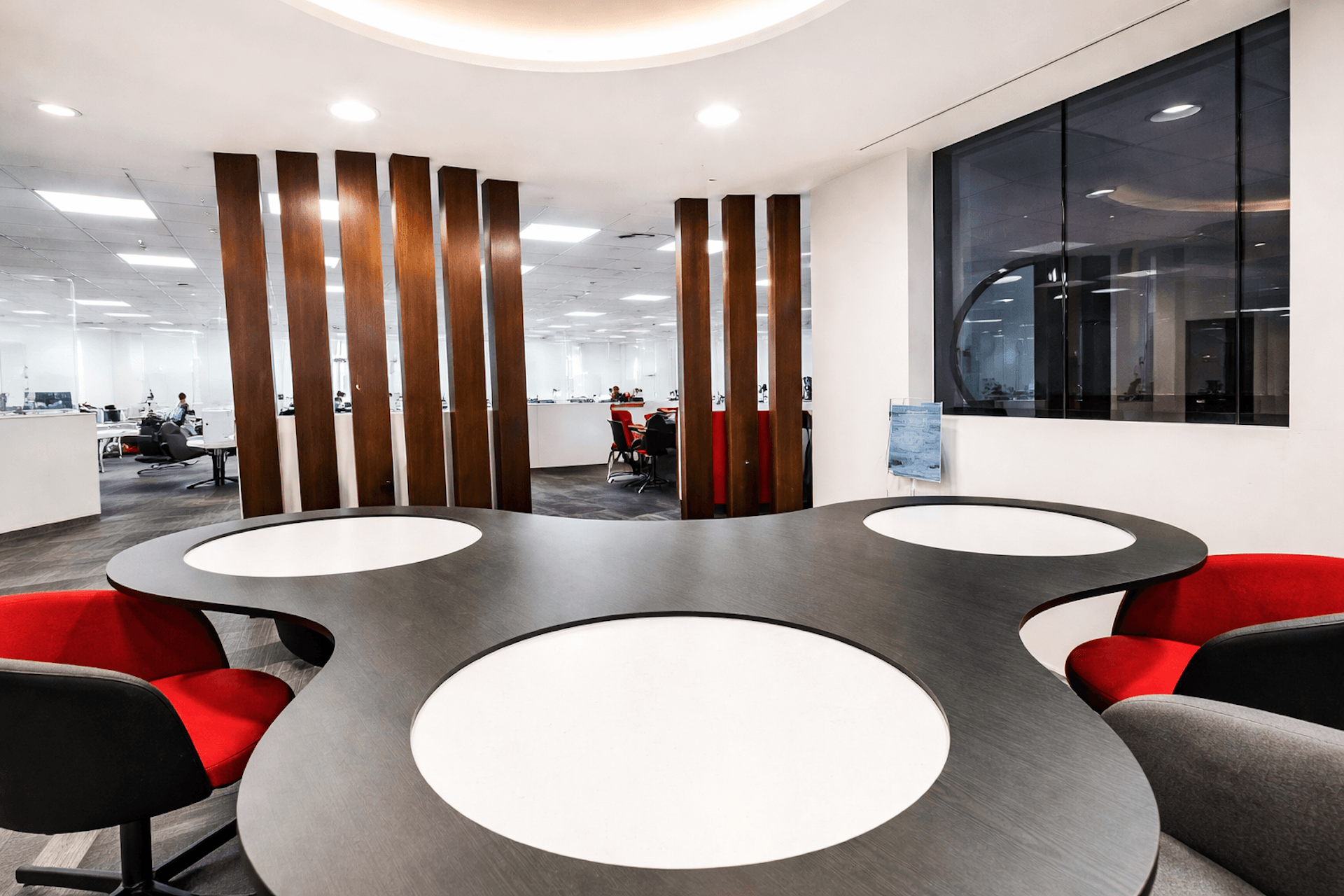 Modern office space with curved tables, red chairs, and wooden dividers