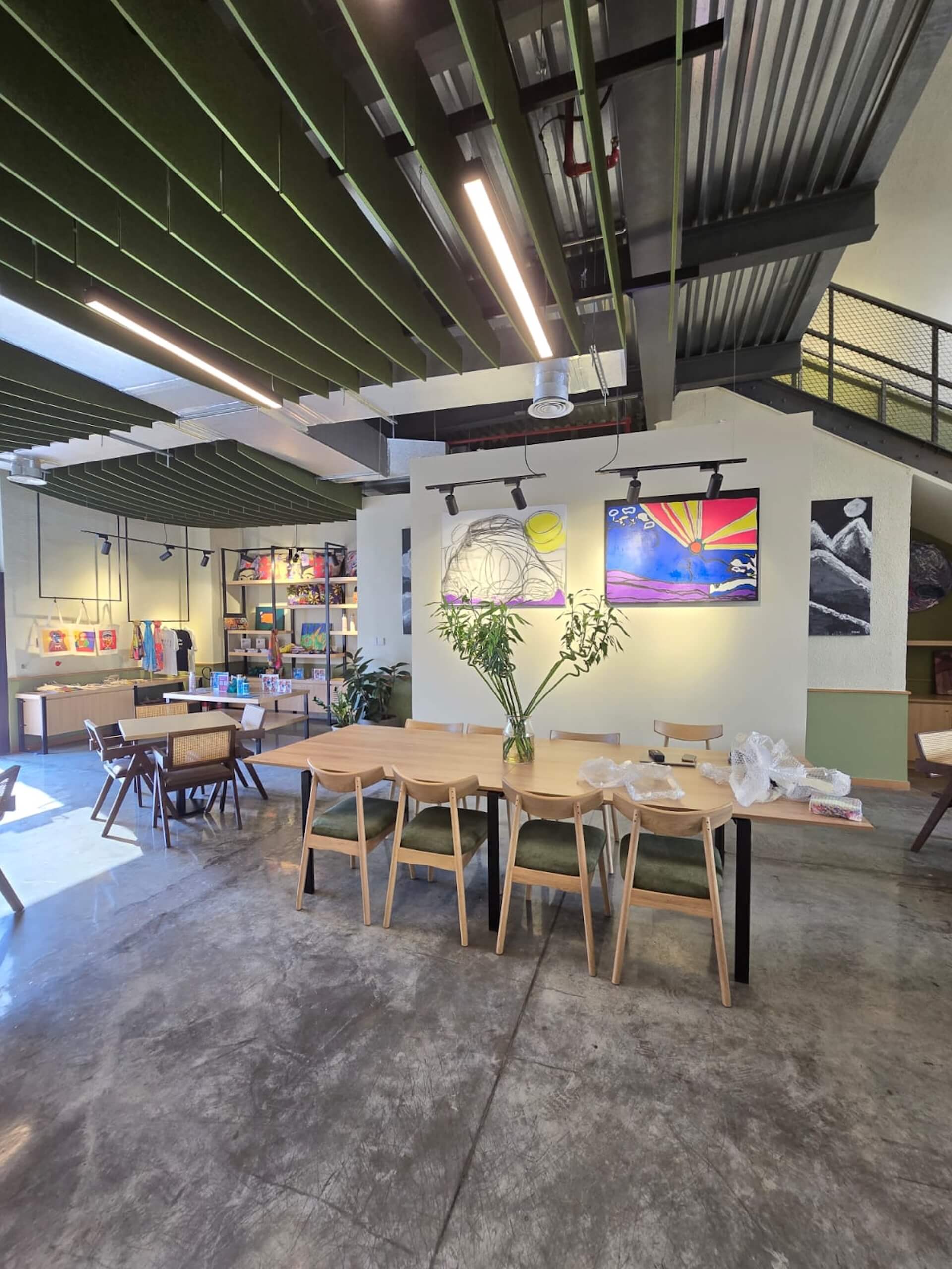Modern office loft with wooden table, chairs, artwork on walls, and industrial ceiling.