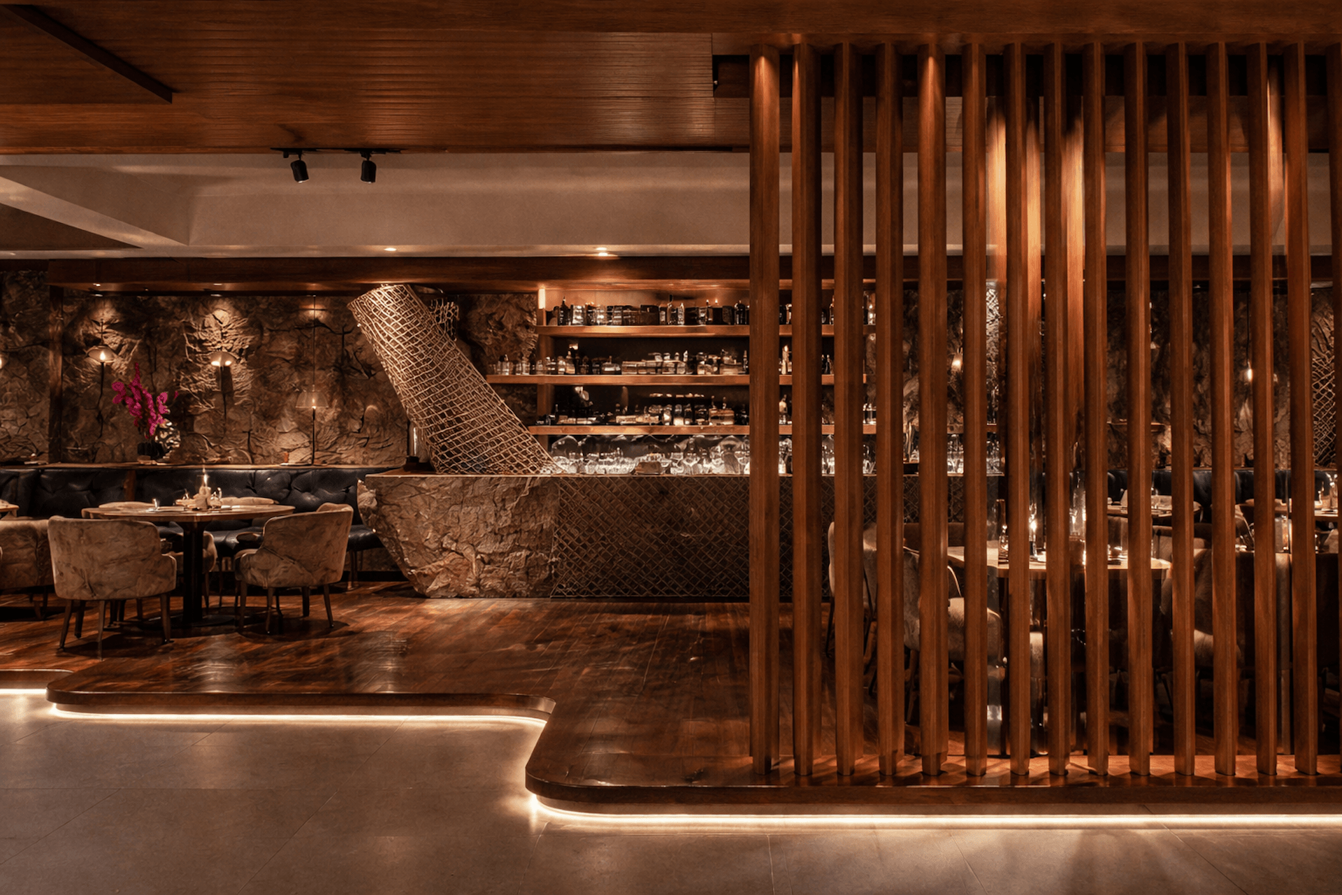 Upscale restaurant interior with wooden partition, bar counter, and elegant dining area.