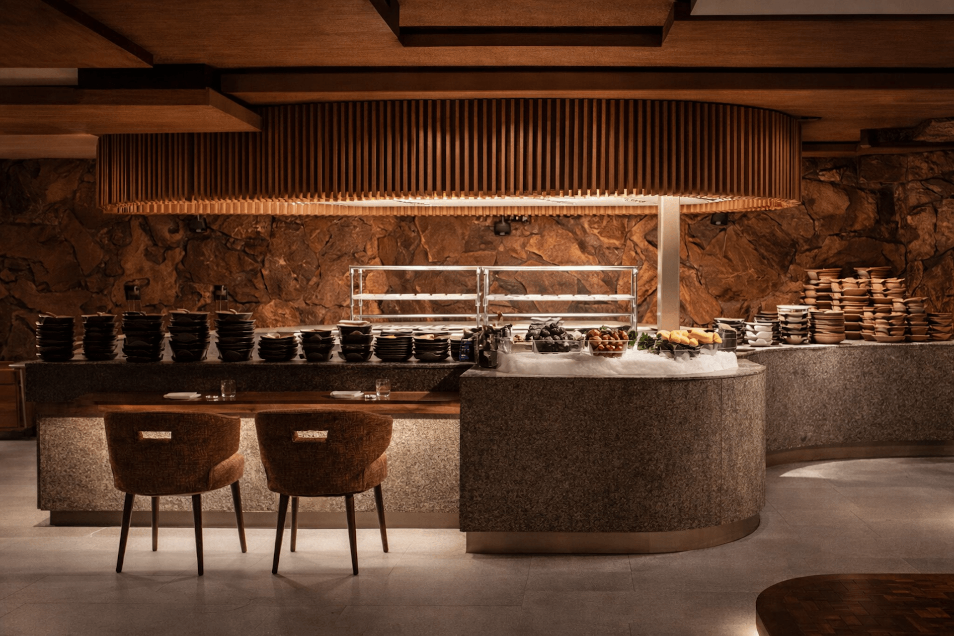 Modern restaurant kitchen with wood beam ceiling, stone walls, and curved counter seating.