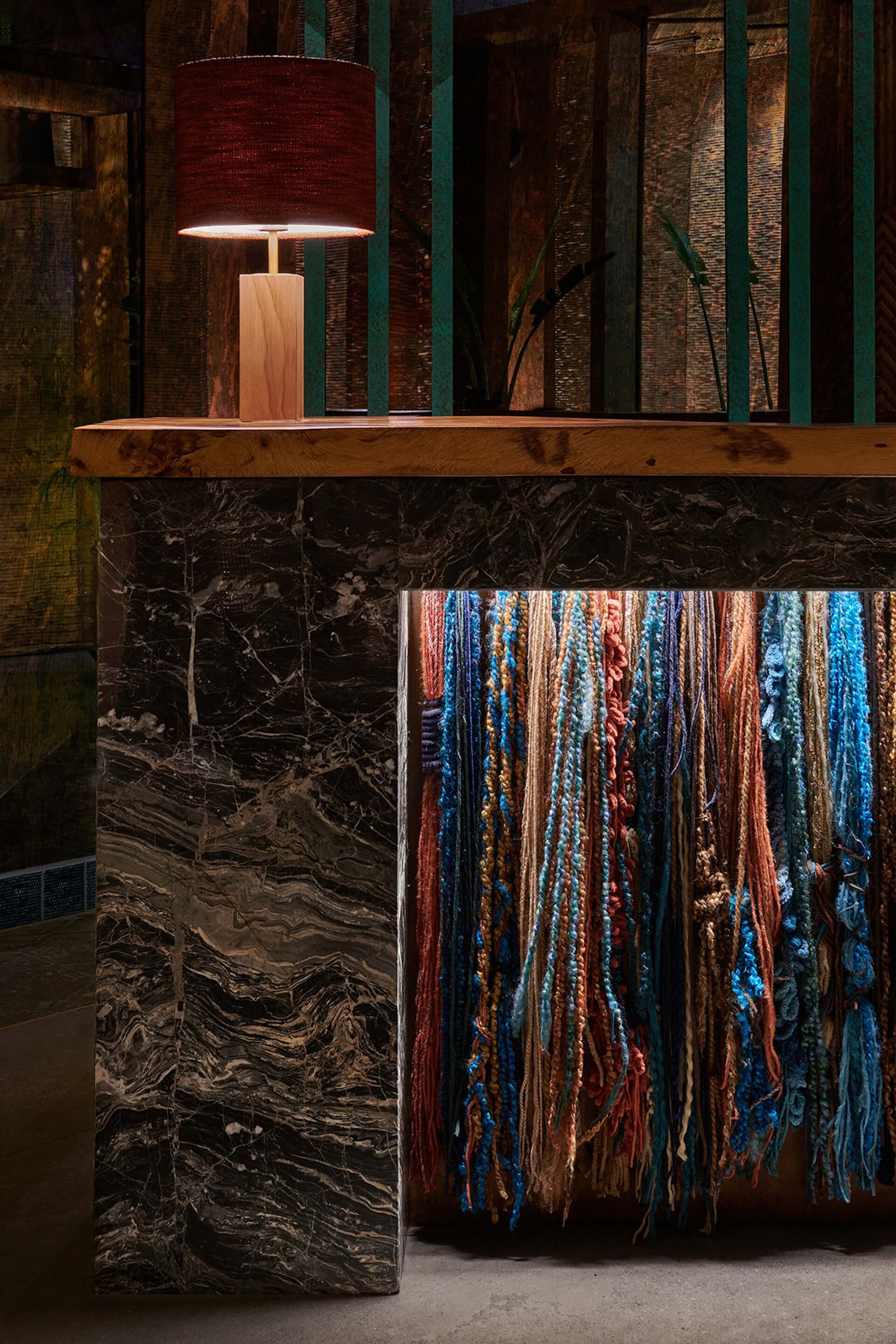 Modern interior display with wooden lamp, textile samples, and dark marble counter against brick wall backdrop.