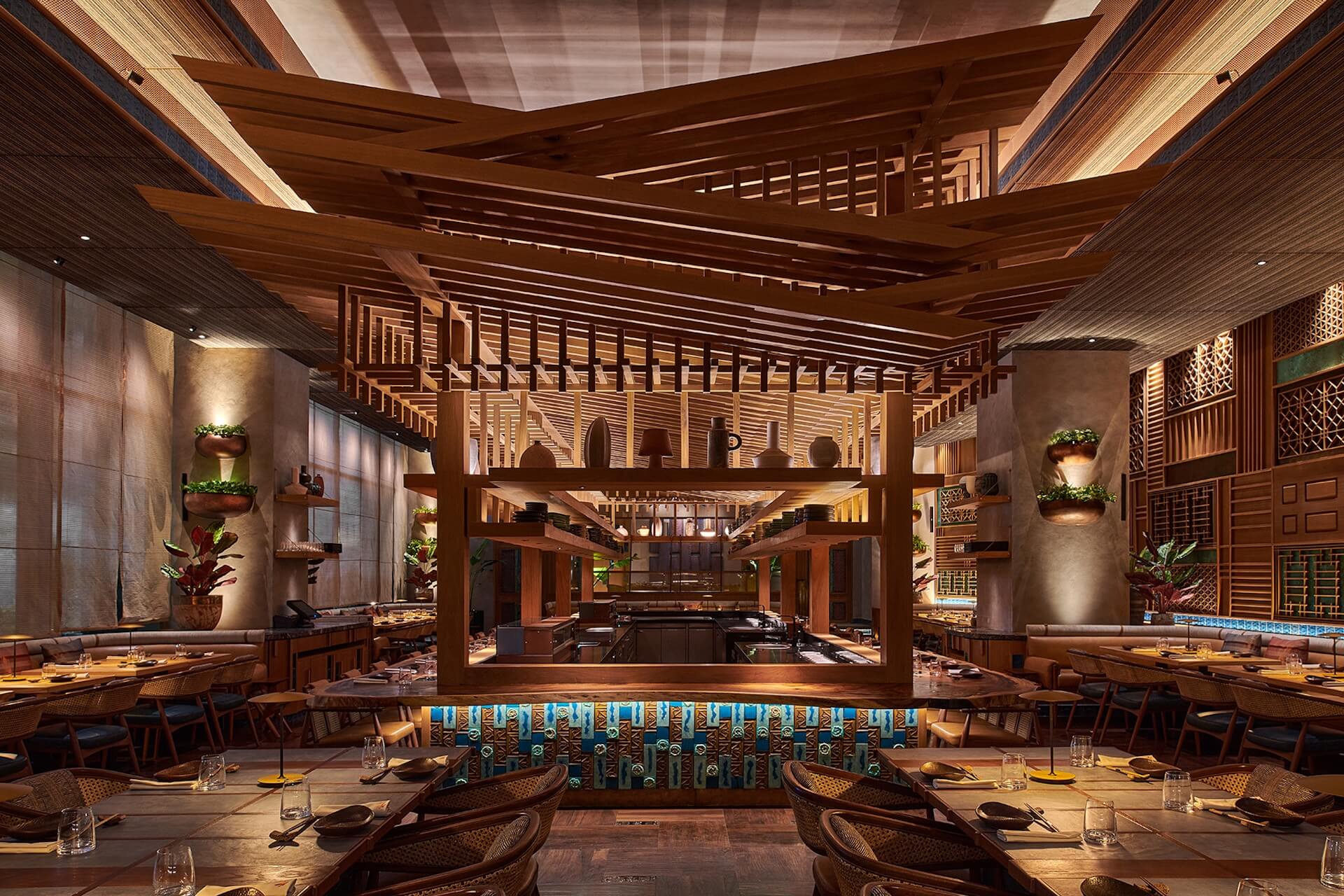 Modern upscale restaurant with wooden beams, central bar, potted plants, and open kitchen concept design.