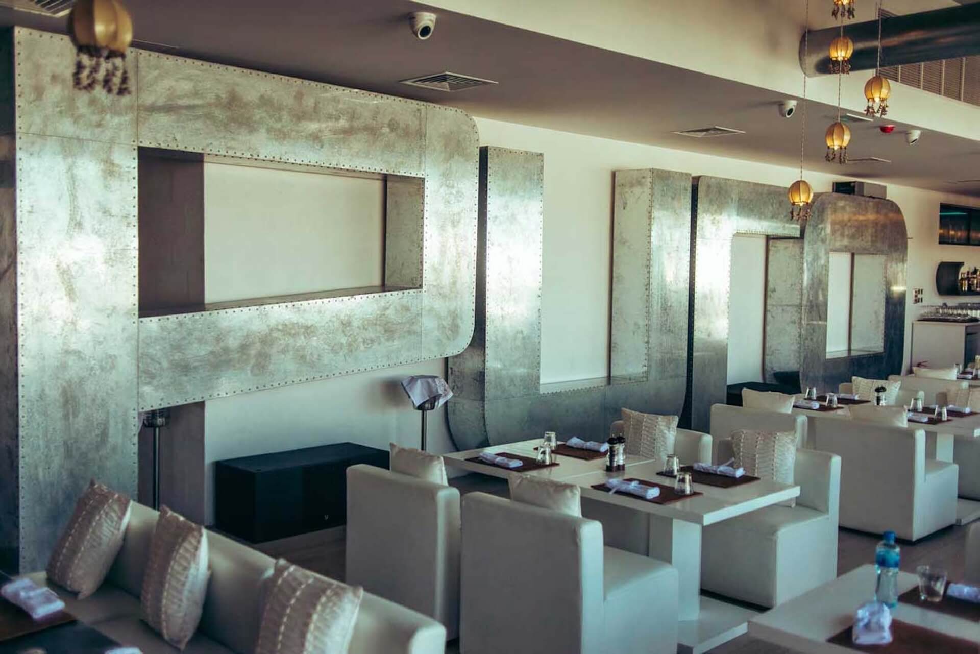 Modern restaurant interior with metallic booth dividers, white seating, and hanging amber pendant lights.