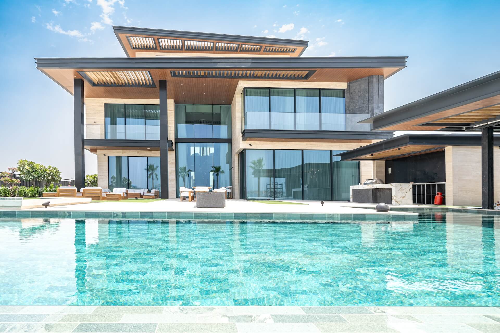 Modern luxury home with swimming pool, large windows, and contemporary architecture under blue sky