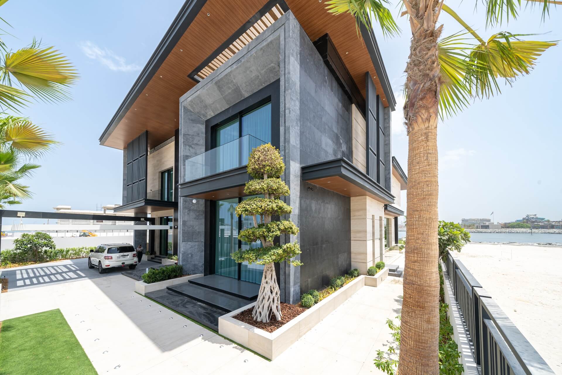 Modern luxury waterfront home with concrete facade, palm trees, and glass balconies.