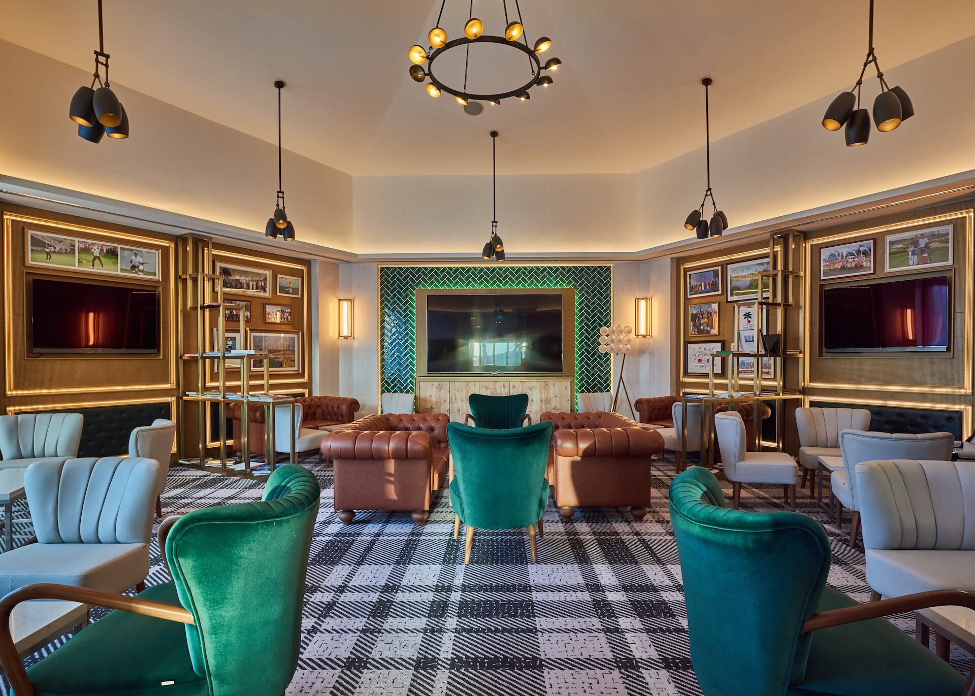Luxury lounge with teal velvet chairs, leather seating, multiple TVs, and modern pendant lighting fixtures.
