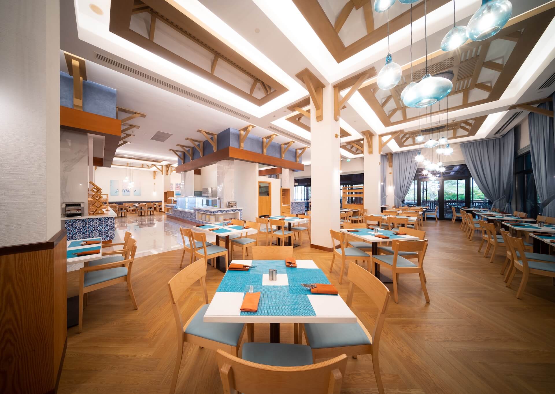 Modern restaurant interior with wooden beams, blue and orange accents, dining tables and skylight ceiling
