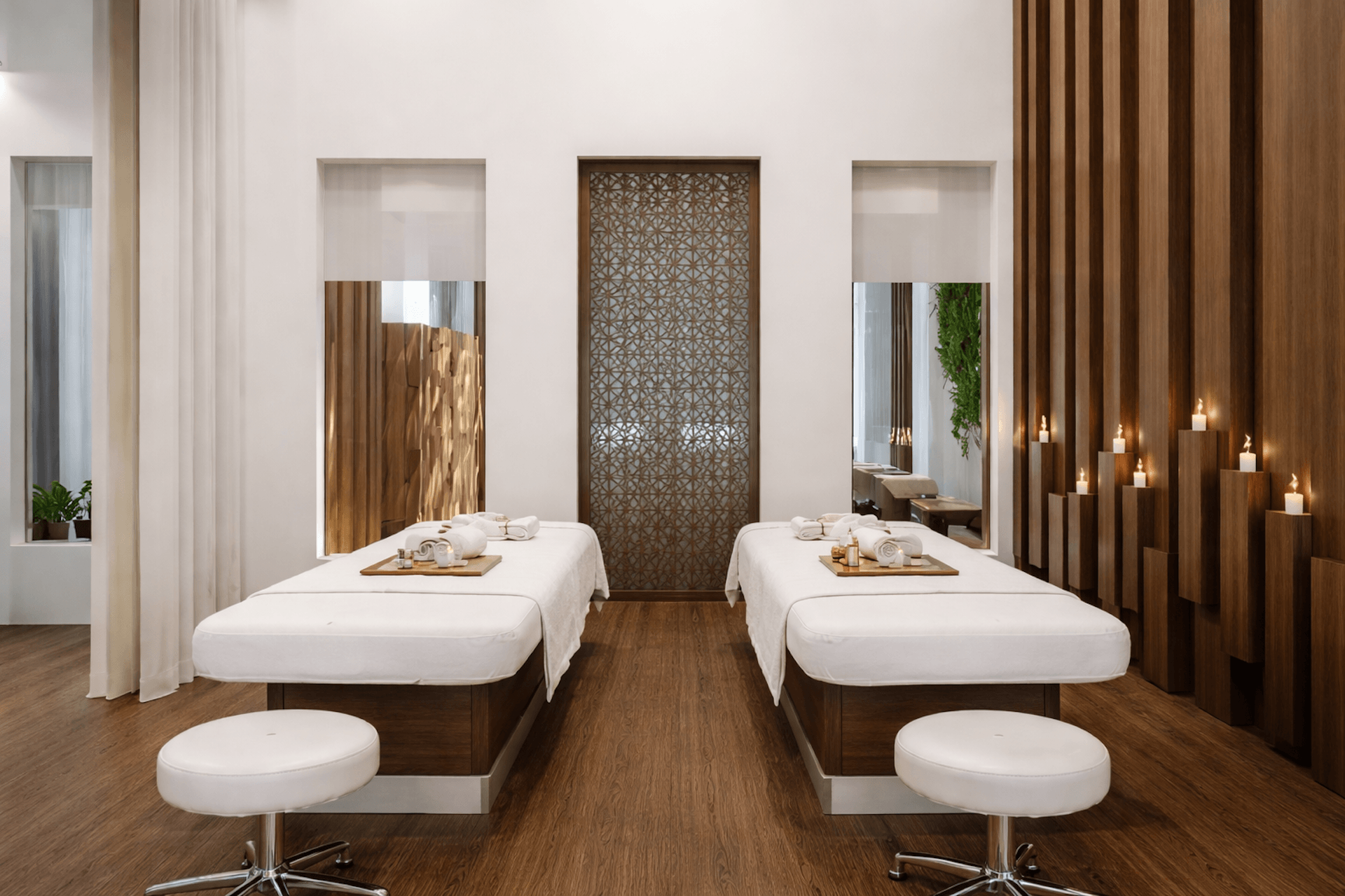 Modern spa treatment room with two massage beds, mirrors, and decorative candles