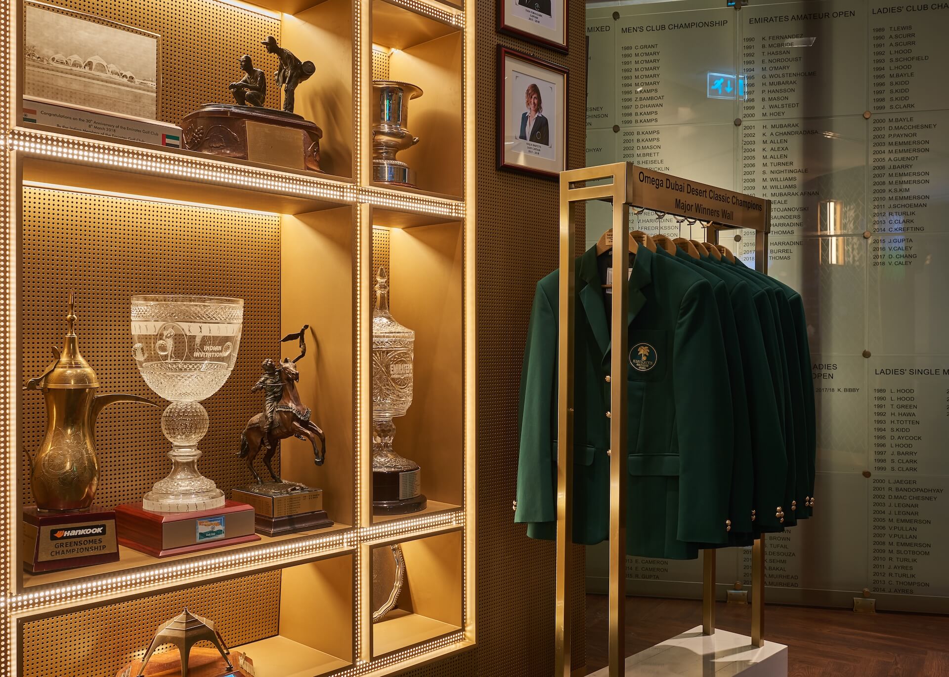 Golf club trophy display with green jackets and championship awards on wall