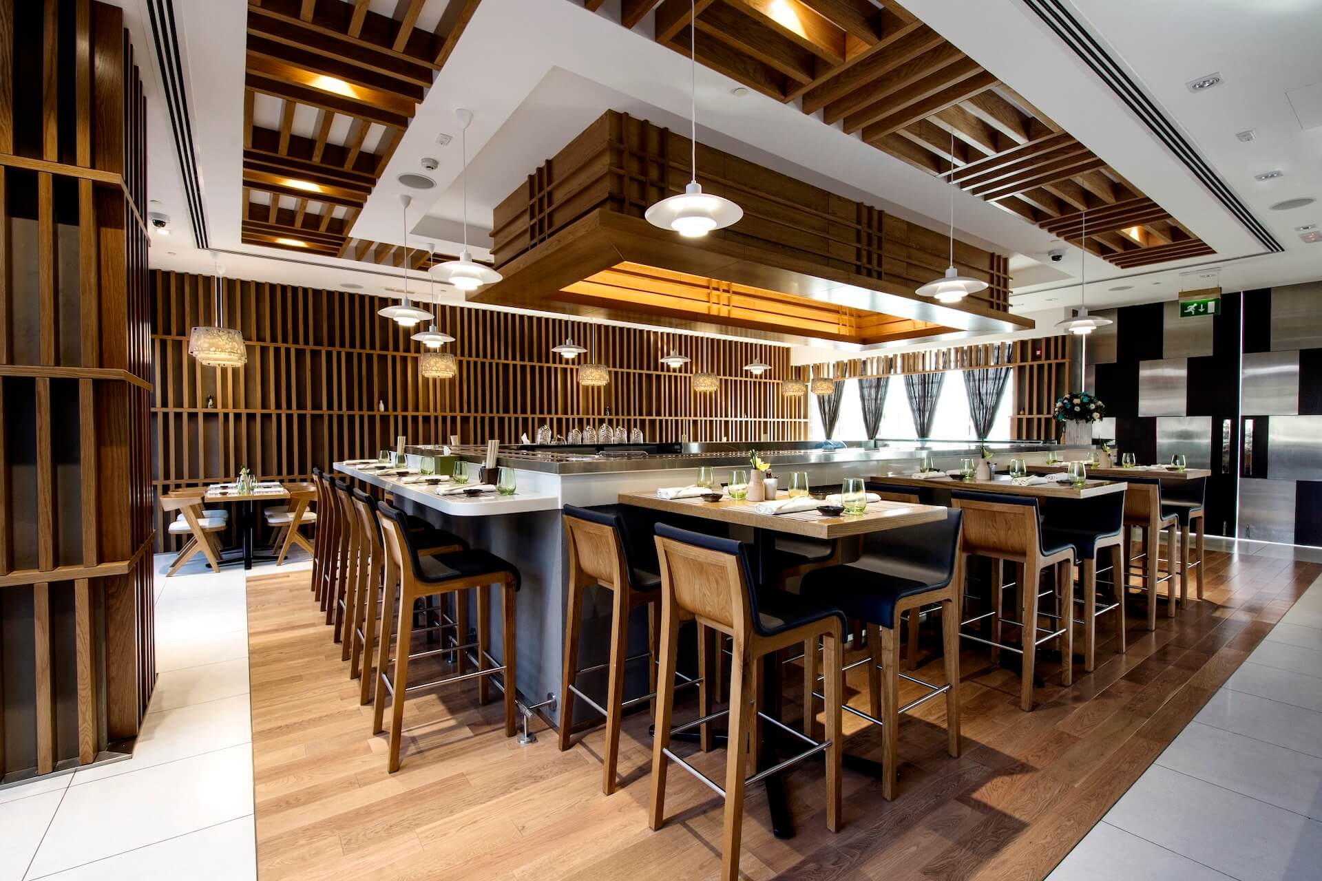 Modern restaurant interior with wood accents, pendant lighting, bar seating, and open kitchen design