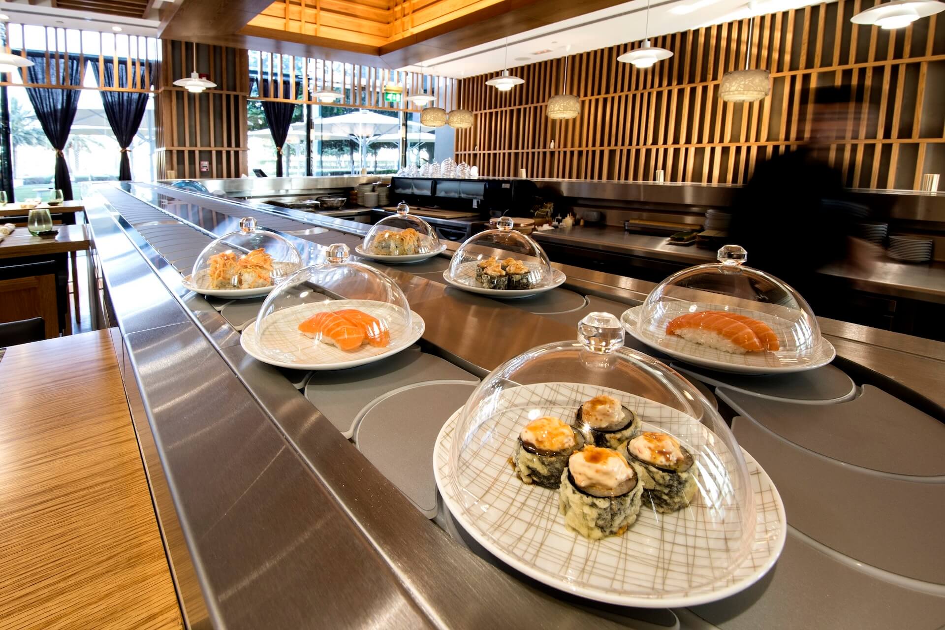 Modern sushi restaurant with plated dishes under glass domes along metal counter