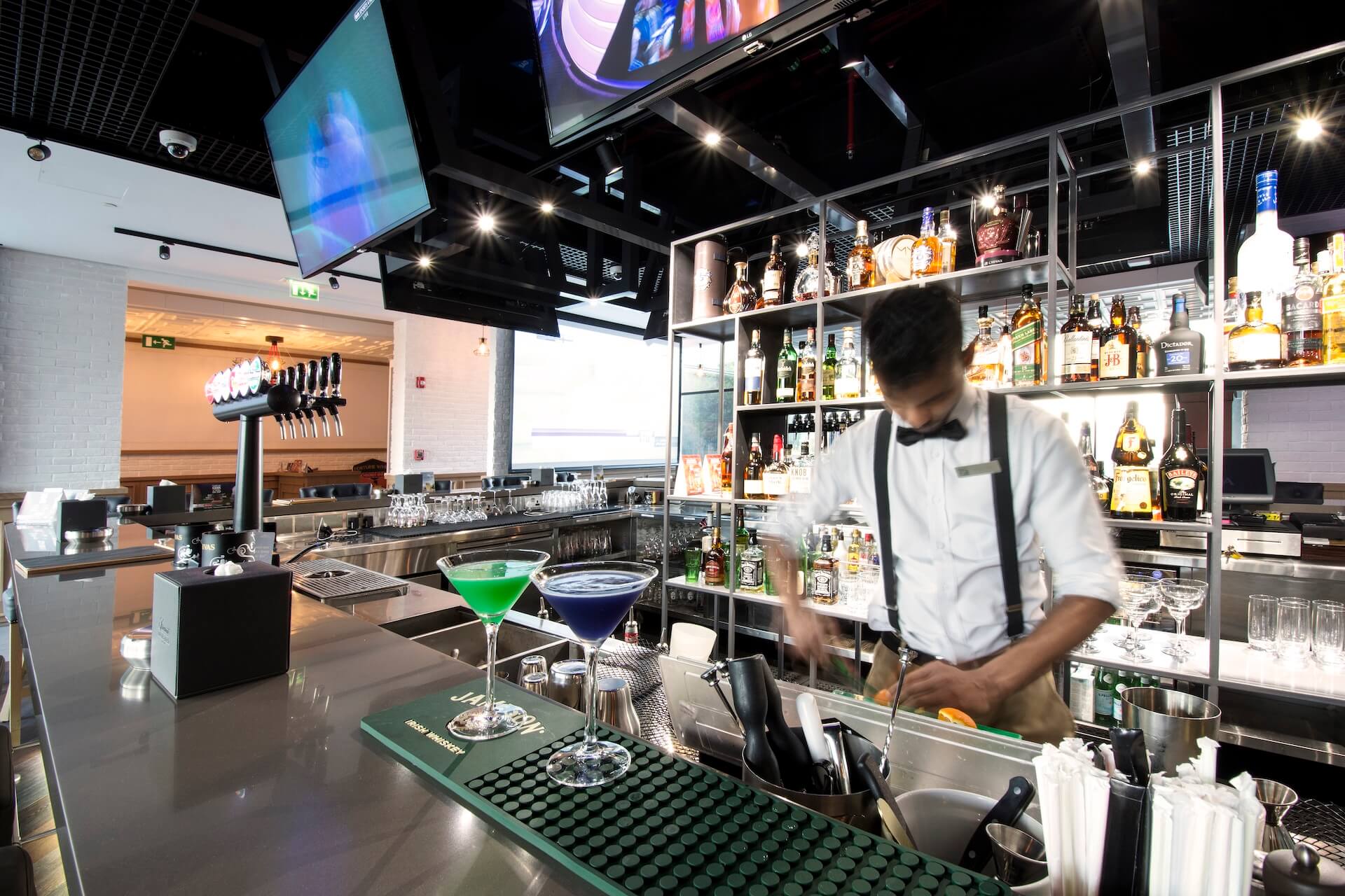 Bartender preparing cocktails at modern bar with colorful drinks and well-stocked shelves