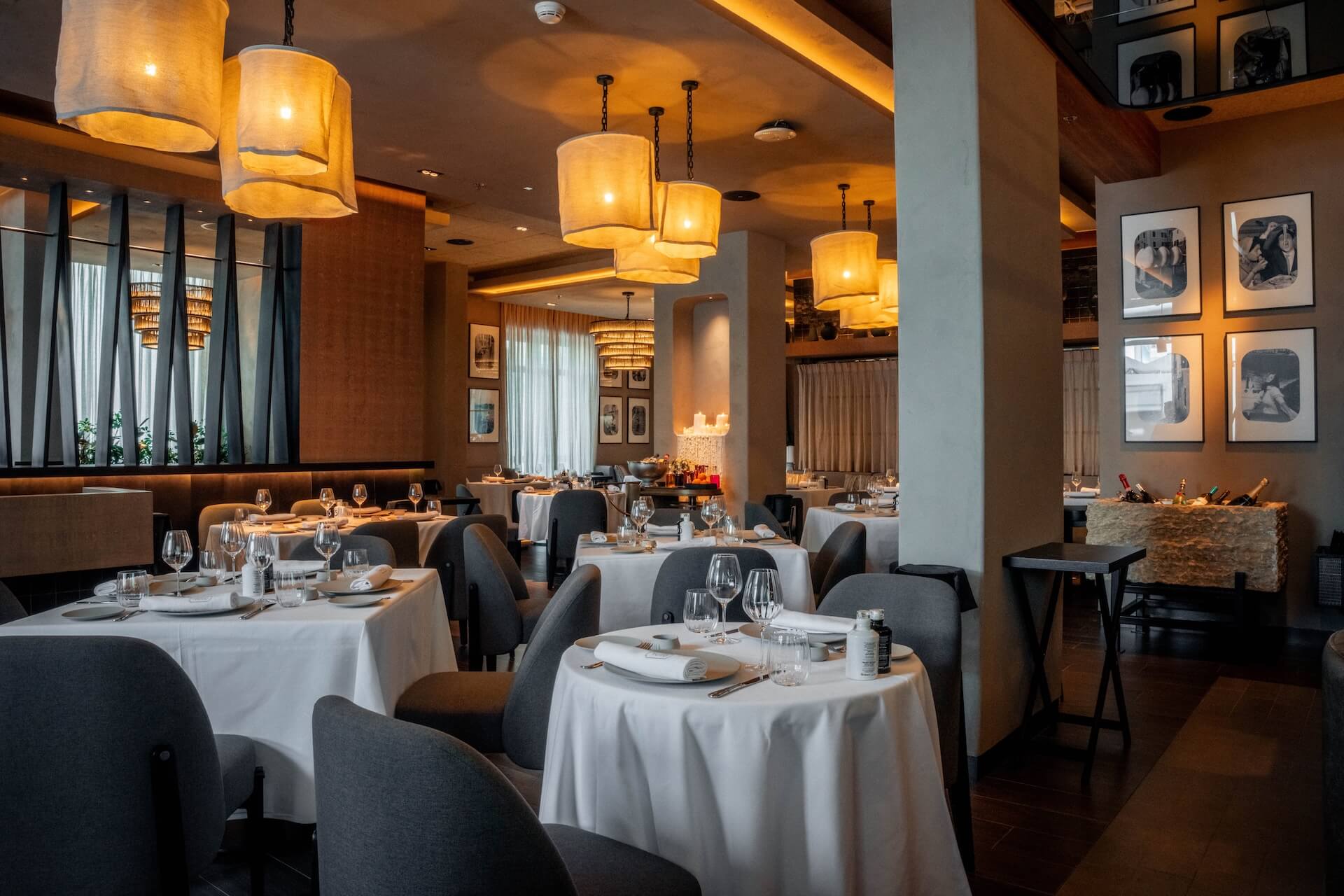 Elegant fine dining restaurant with warm lighting, round tables with white linens, and modern decor.