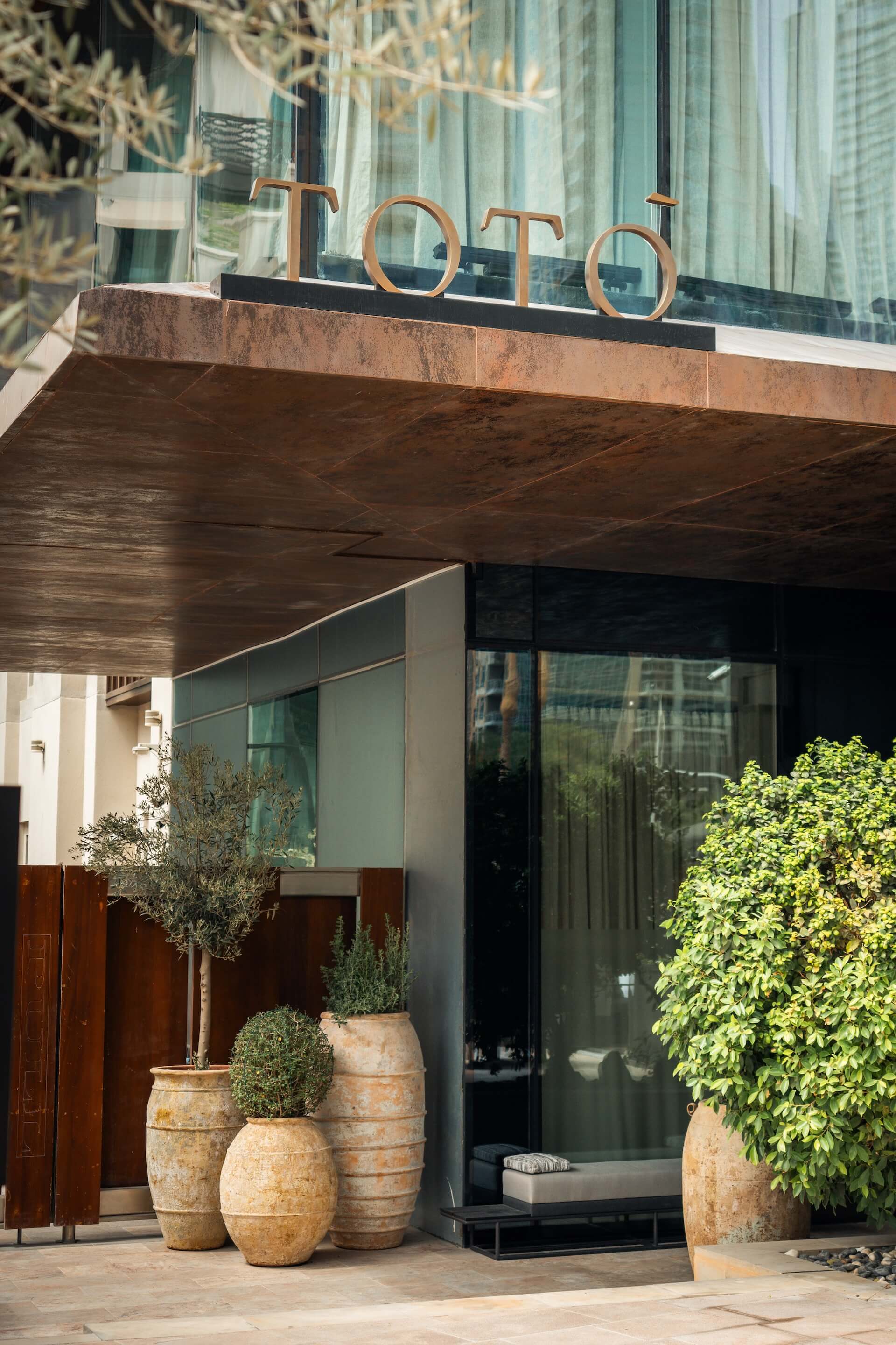 Modern storefront with copper lettering, terra cotta planters, and glass entrance doors.