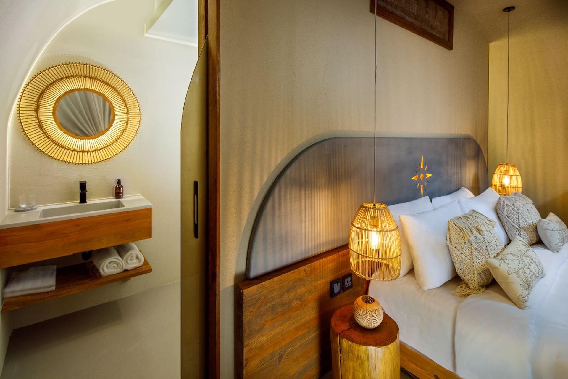 Modern hotel bedroom with wooden furnishings, woven pendant lights, and gold-framed mirror.
