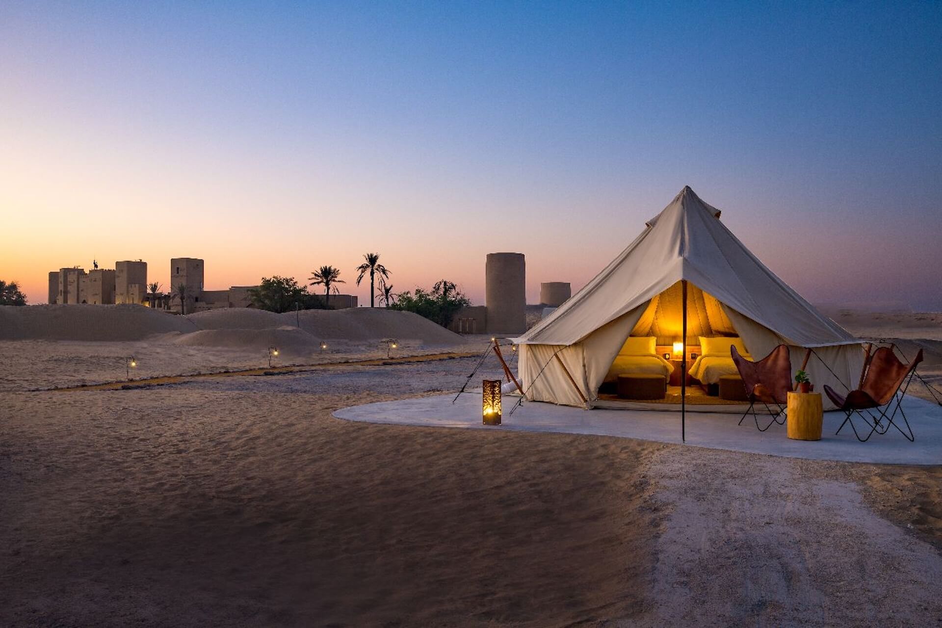 Luxurious tent glowing at dusk with ancient ruins silhouetted under twilight sky