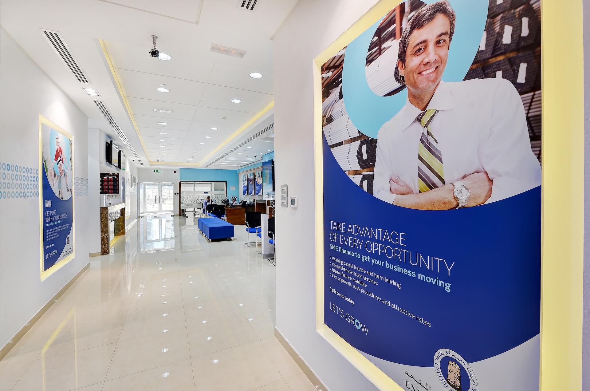 Modern bank interior with blue and yellow branding, business opportunity promotional signage displayed.