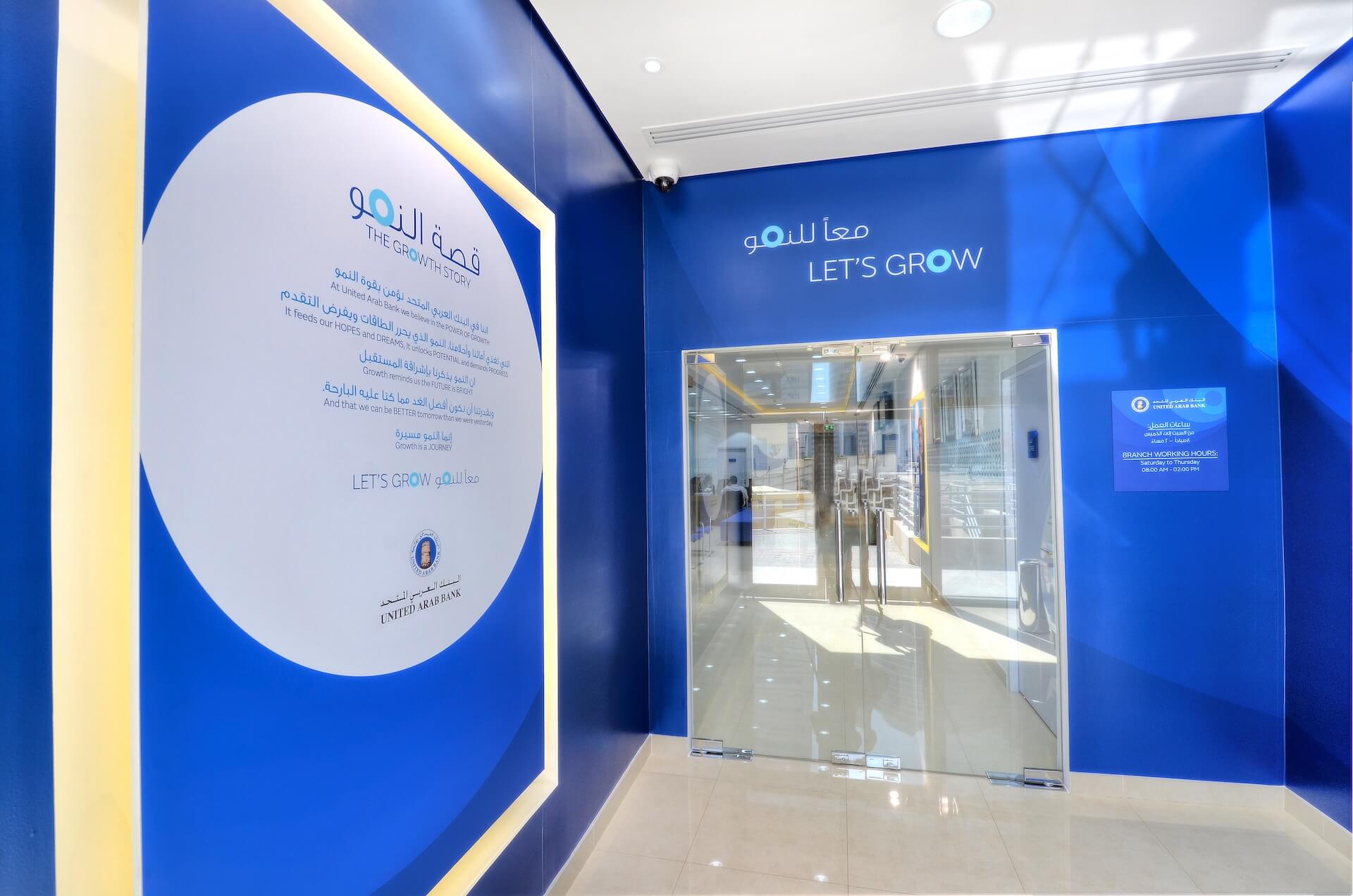 Modern bank branch entrance with blue walls, glass doors, and "Let's Grow" signage